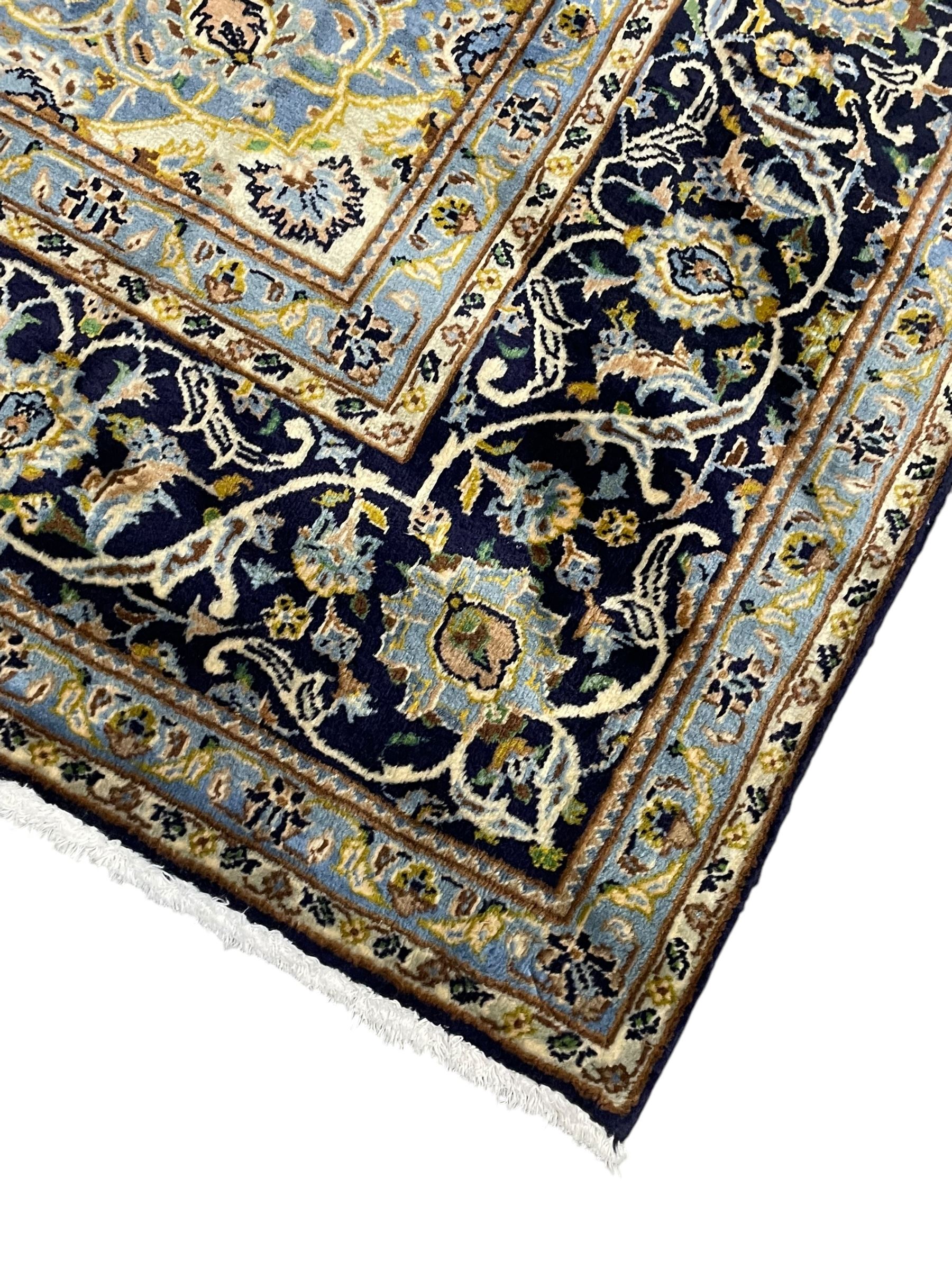 Persian Kashan indigo ground rug, central floral pattern pole medallion, the field decorated with palmettes united by trailing branches, repeating floral pattern border within guard stripes
