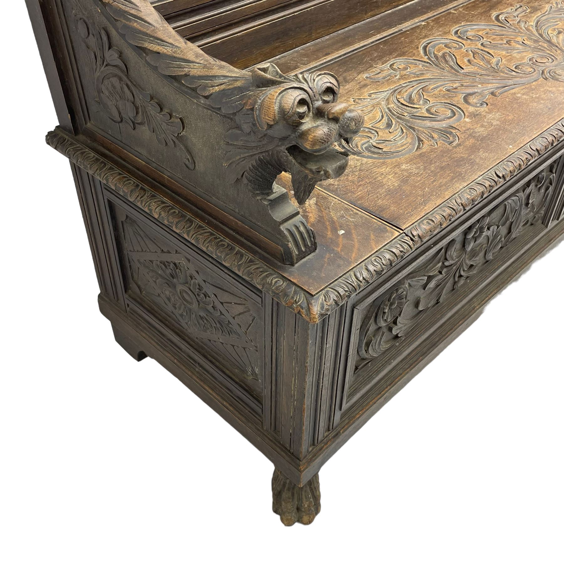 19th century oak hall bench, dentil cresting rail over moulded frame with panelled back carved with fire-breathing mythical beasts and central acanthus leaf motif, scroll carved down-sweeping arms carved with grotesque masks with scrolled foliage and shells, hinged box seat carved with scrolling foliage over panelled front with further carved foliage decoration, on paw carved front feet 