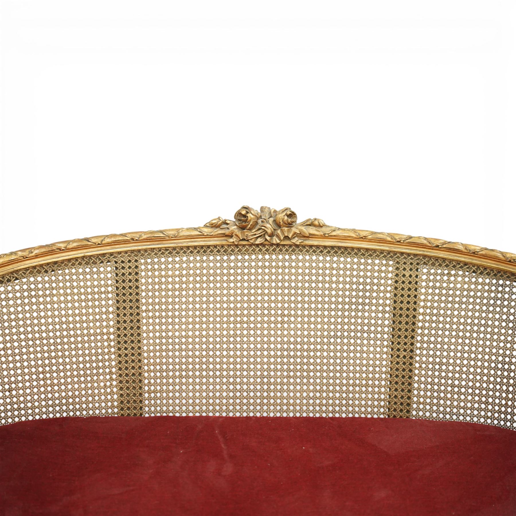 19th century giltwood and gesso settee, with shaped crest rail centred by carved floral detail, the cane back with vertical divisions, upholstered seat with loose cushion, raised on fluted tapering legs