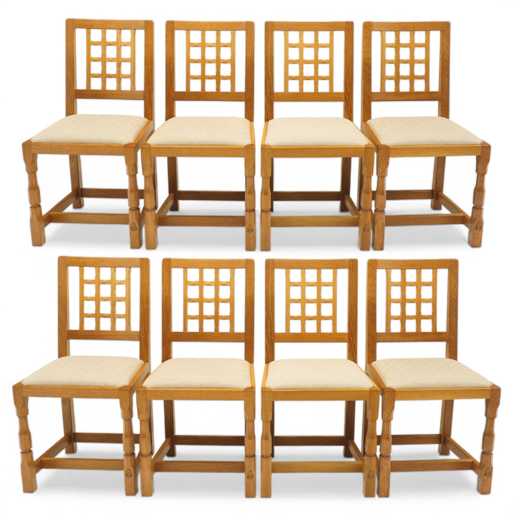 Knightman - eight oak dining chairs, the rectangular back with square section lattice splat enclosed by straight stiles and top rail, drop in upholstered seat in pale patterned fabric, raised on square section legs with chamfered detailing united by stretchers, with carved knight signature, by Horace Knight of Thirsk