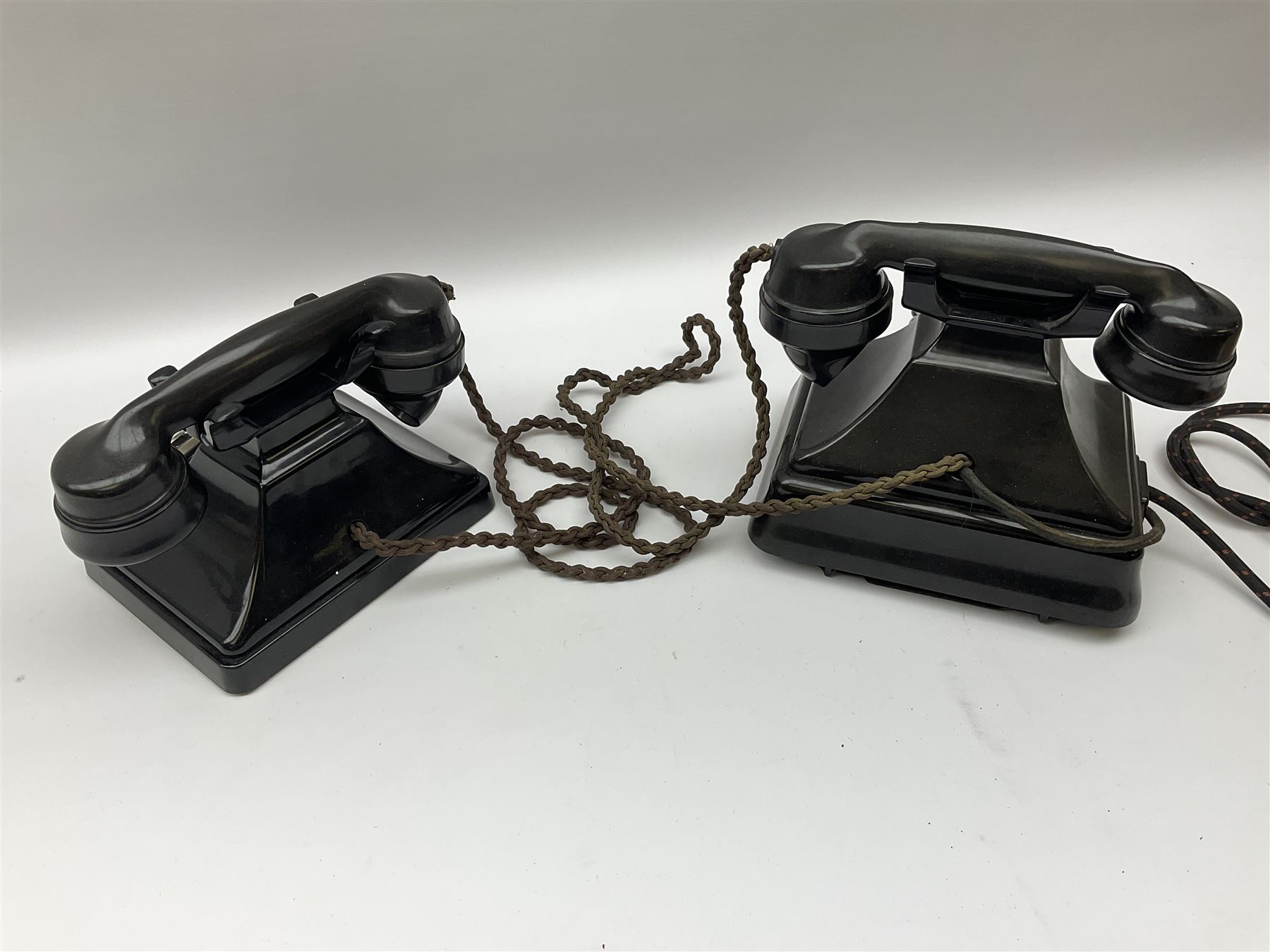 Two black Bakelite telephones of pyramid form with rotary dials, comprising The Telephone Demonstration Set model. 6al with base drawer and light bulb, and another larger with G.P.O FWR 58/2 stamped marks beneath, largest H18cm W20cm D16cm