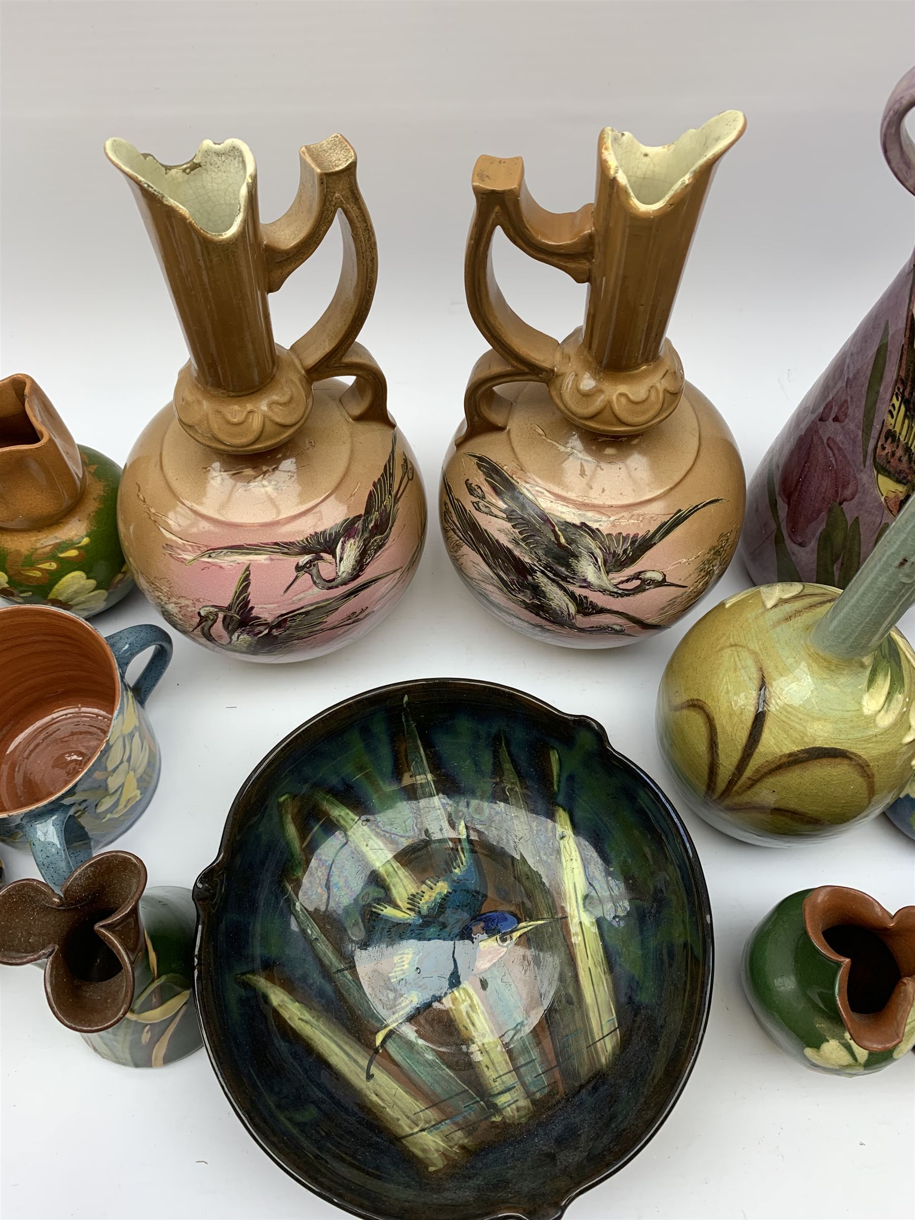 Collection of Devon pottery all having floral slip decoration and include Aller Vale, Watcombe, possibly some Longpark, and other unmarked pieces, tallest H25cm together with a pair of T. Forester jugs hand-painted with cranes and two further Devon pottery pieces, both hand-plated with birds 
