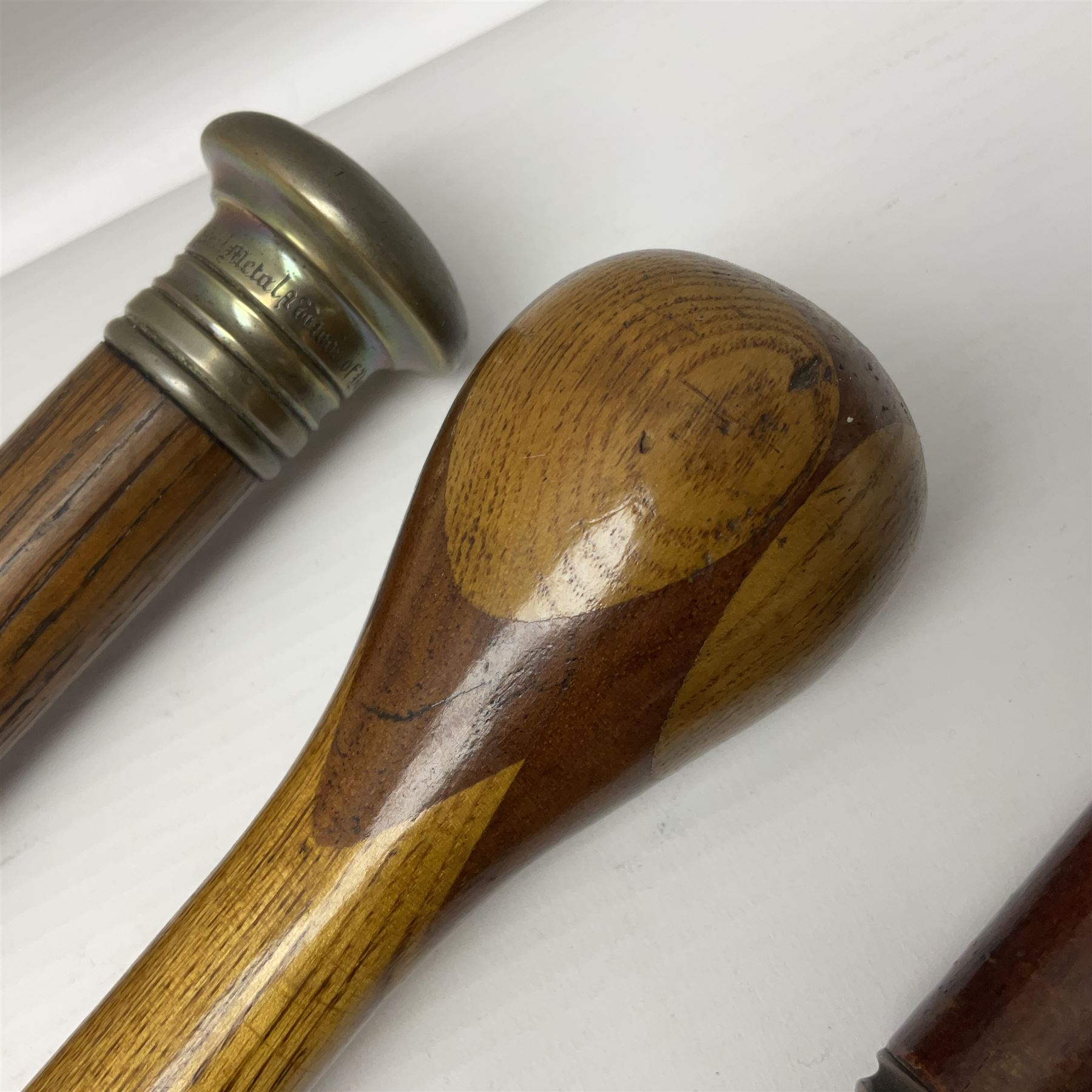 Three early 20th century walking sticks, to include a smoking pipe walking stick, the cane opening to reveal a concealed pipe, and a wooden walking cane, the metal cover with inscription 'bell metal and wood of York Minster, Burnt May 20 1840, and a turned wooden walking stick, with marquetry checkerboard pommel, tallest L90cm