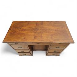 Early 20th-century Georgian-style walnut kneehole desk, the rectangular top with feather cross-banded border, above an arrangement of eight short drawers flanking a central cupboard door, fitted with brass backplate handles, raised on bracket feet