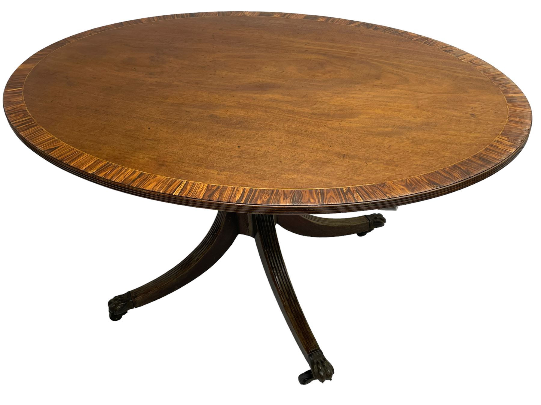 George III mahogany breakfast table, the oval top with a kingwood band and boxwood stringing, raised on a turned vasiform pedestal terminating in a fluted sabre tripod base with hairy paw feet and castors