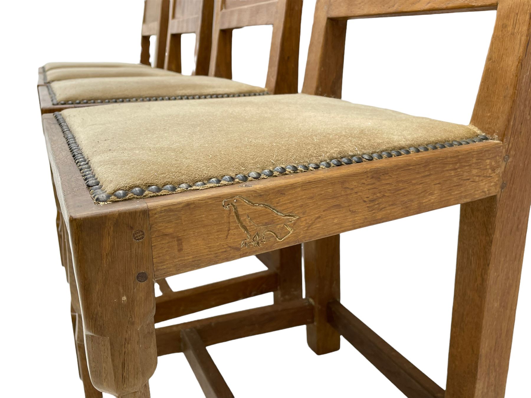 'Eagleman' set four oak dining chairs, adzed panelled backs, upholstered seats with stud work band, the side rails relief carved with inset eagle signature, shaped octagonal supports joined by stretchers, by Albert Jeffray of Sessay, Thirsk