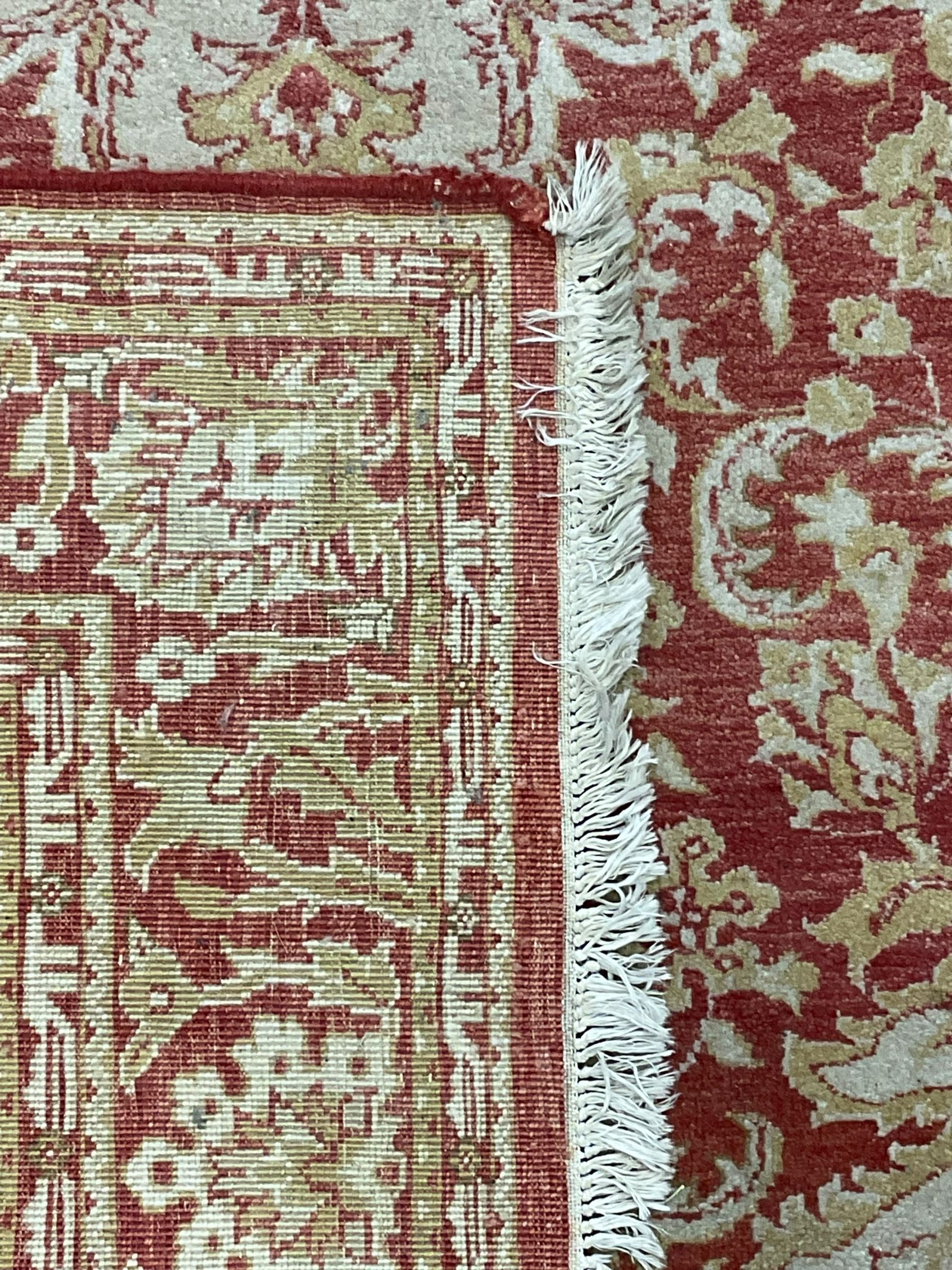 Persian design beige and crimson ground rug, the field decorated with interlacing scrolled foliage, repeating border within guard stripes 
