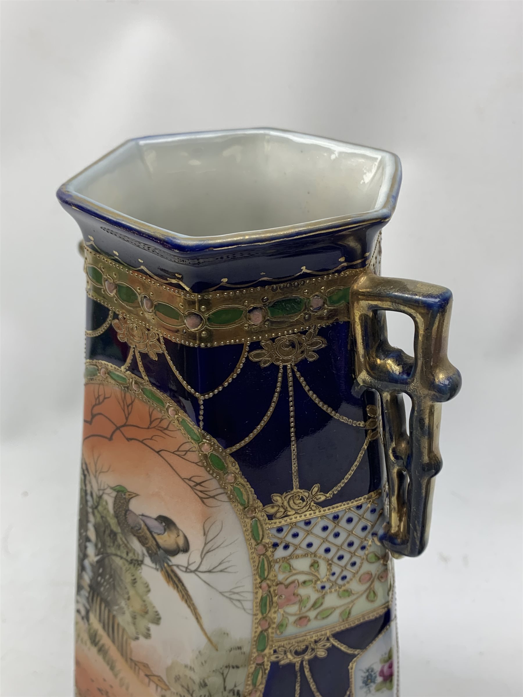 A pair of Japanese Nippon Kinjo vases, of tapering hexagonal form with twin stylised handles, the cobalt blue ground with oval hand painted panels to front and verso depicting landscapes, further detailed with smaller floral bands and panels and heightened with gilt, each with mark beneath, H30.5cm.  