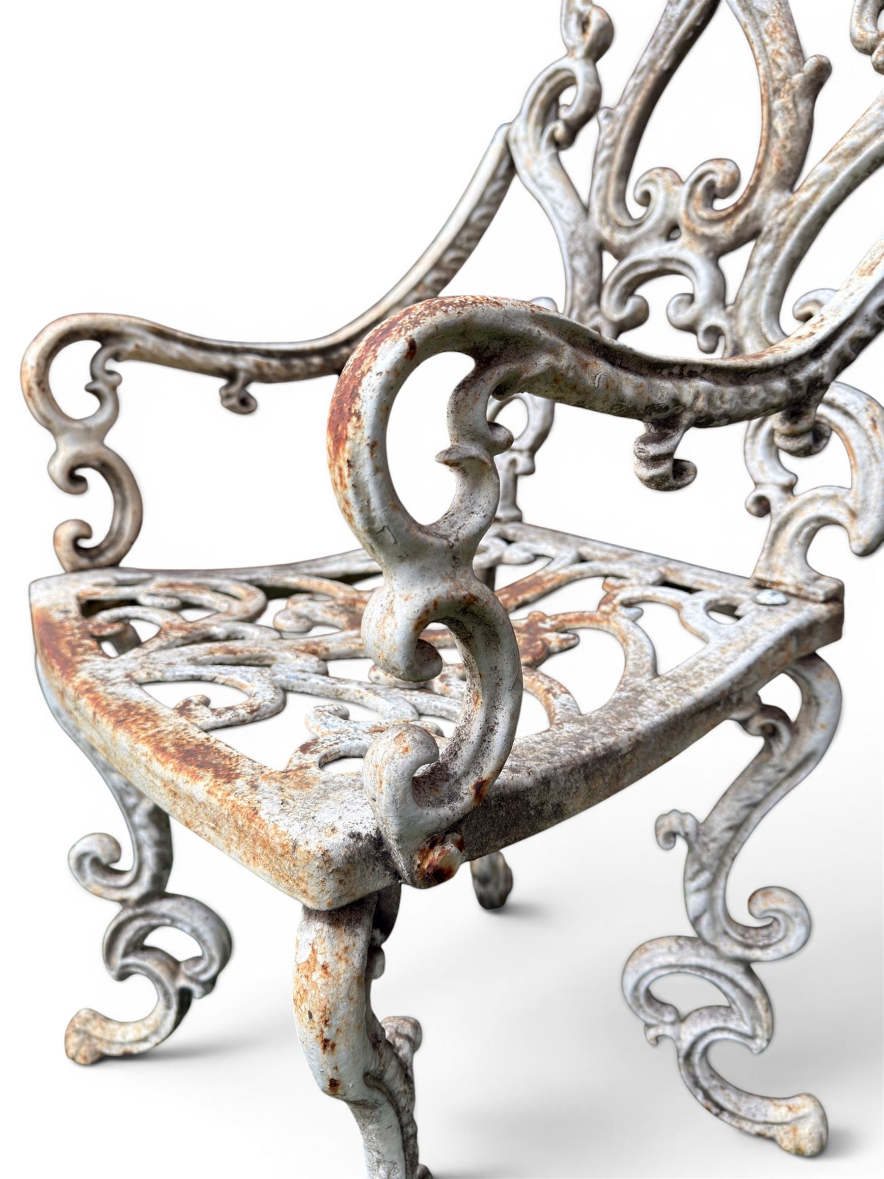 Pair of Victorian cast iron garden chairs, the ornate pierced back of scrolling foliate design, scrolling arm terminals over splayed supports formed of C and S-scrolls, in distressed white painted finish