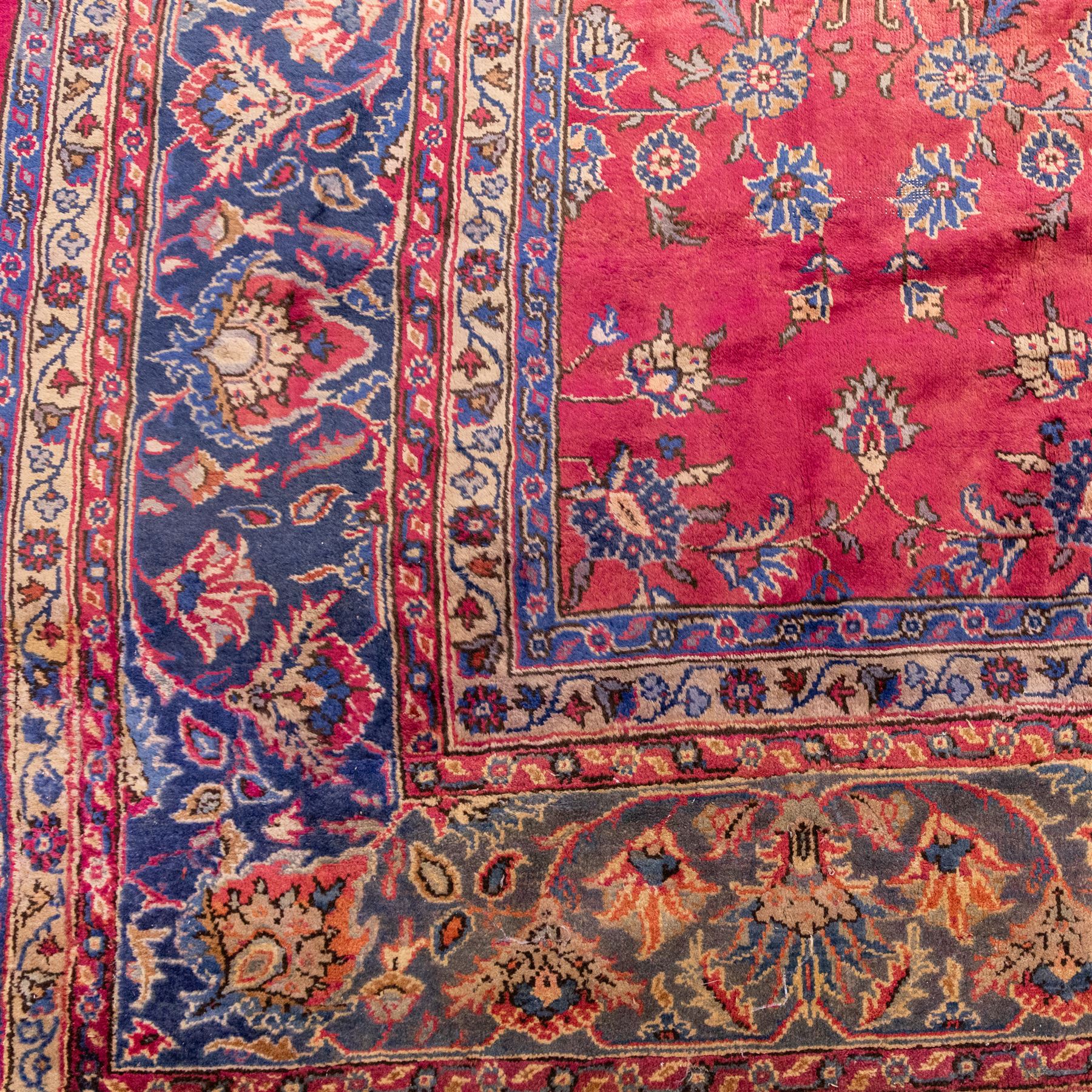 Large Persian-style mahal-type hand-knotted carpet, of rectangular form with a deep crimson field decorated with an all-over arrangement of stylized floral sprays and palmettes, with a central subtle medallion composition enclosed by a dark navy main border of scrolling floral motifs between narrow guard stripes with fringe ends 