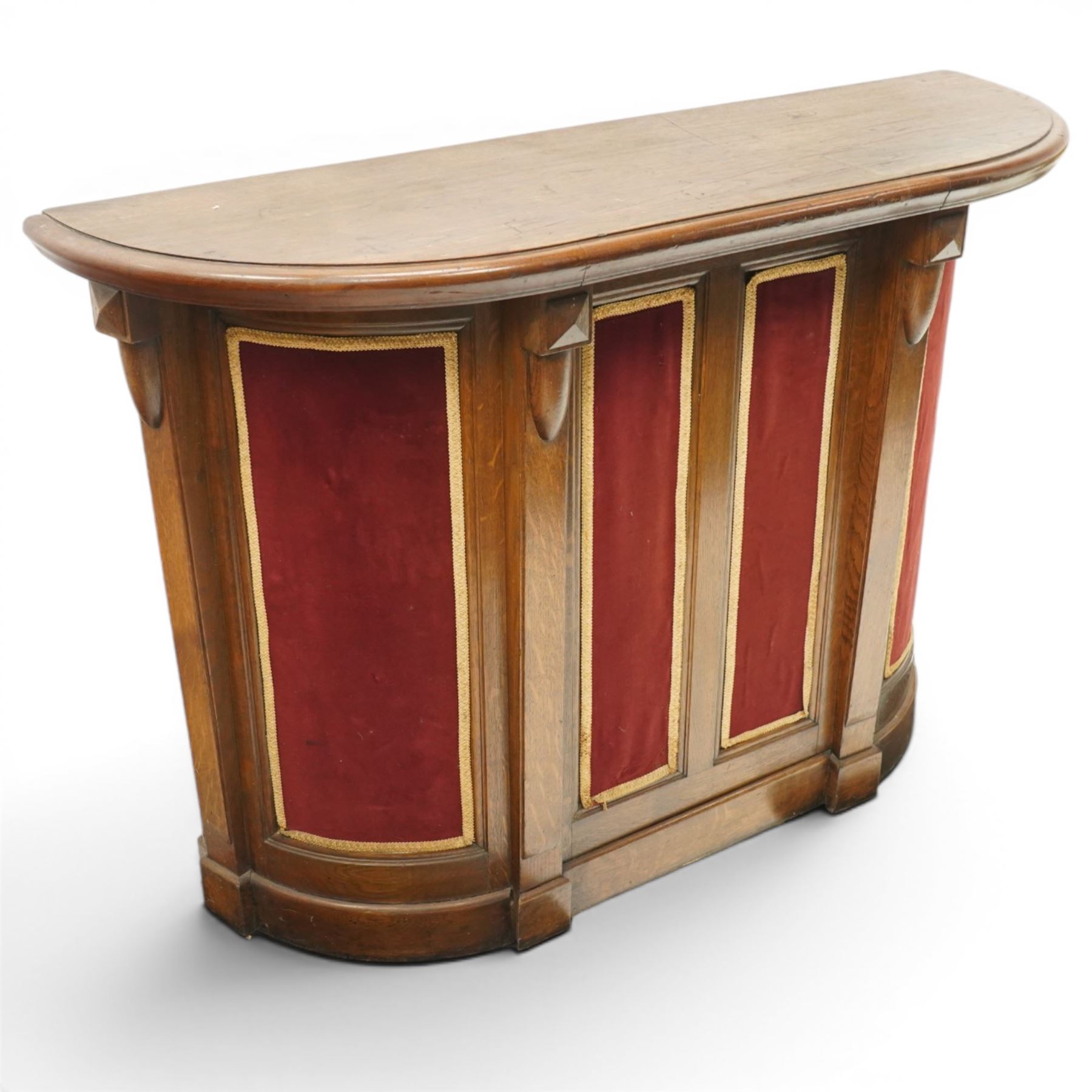 Arts & Crafts oak D-shaped bar, moulded edged counter above a front with velvet applied panels, the back with shelving, raised on a plinth base