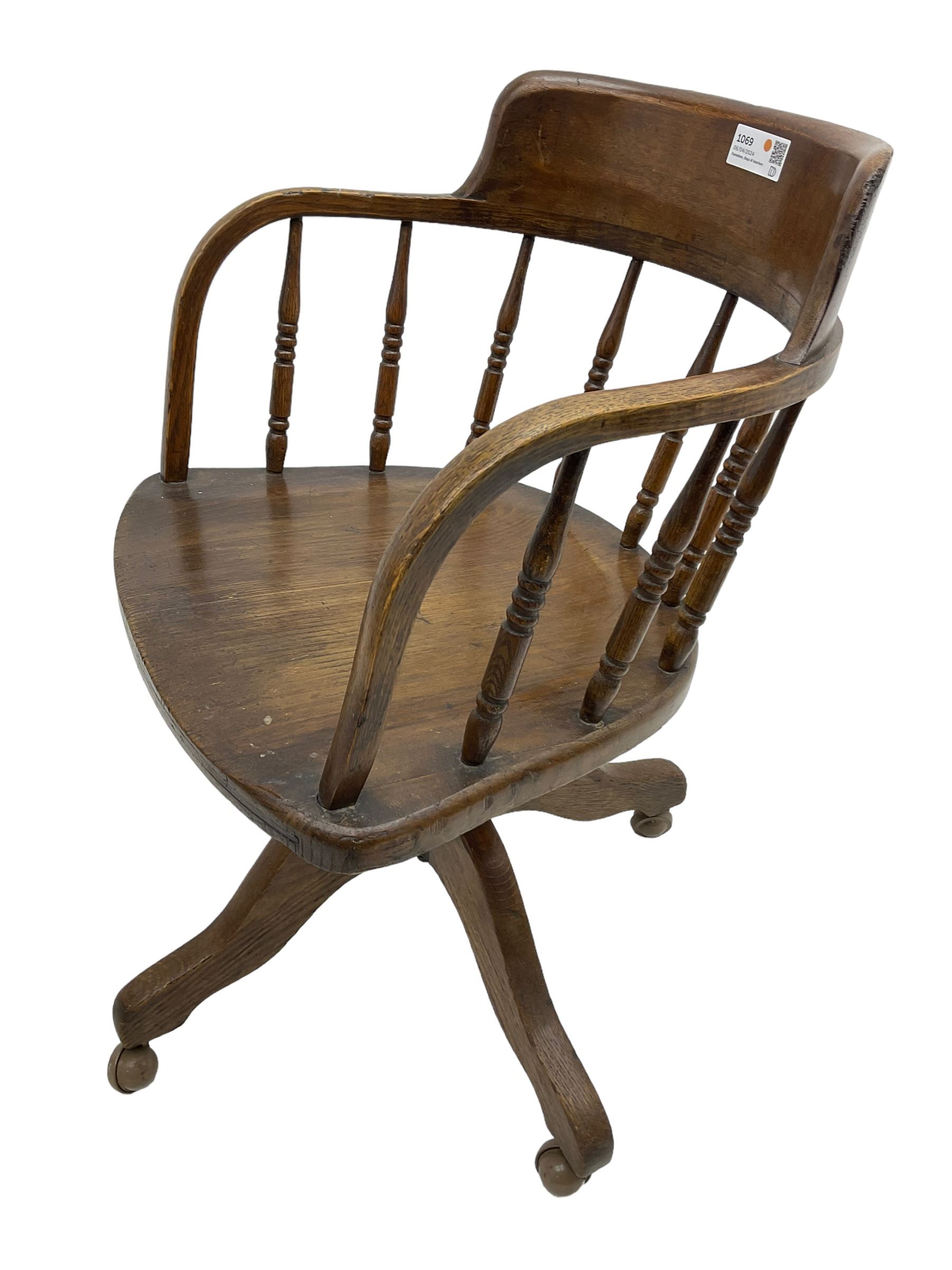 Early 20th century oak framed swivel Captain's chair, tub shaped back with turned spindle supports over saddle shaped seat, quadriform base on castors