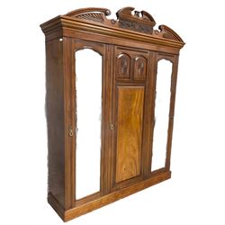 Victorian mahogany triple wardrobe, the pediment relief carved with urn and linen swags, the central panelled door carved with two fan motifs enclosing slides and drawers, two mirror glazed doors with bevelled plates enclosing hangings space and drawers, plinth base