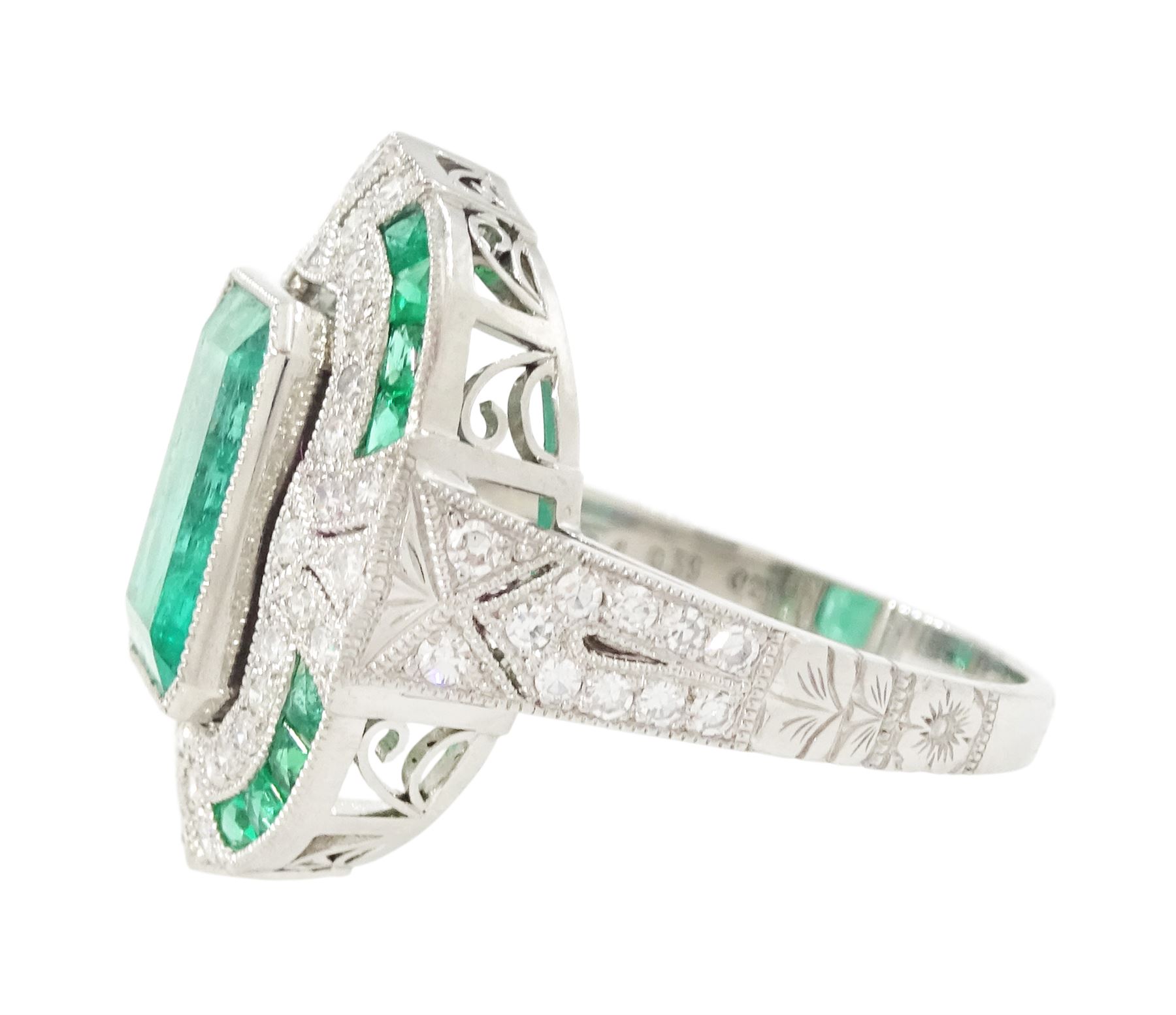 Platinum emerald and diamond milgrain set dress ring, single octagonal cut emerald of 2.40 carat, surrounded by single cut diamonds and a border of calibre cut emeralds, with fancy pierced design gallery diamond and engraved flower head shoulders, stamped 850 Plat