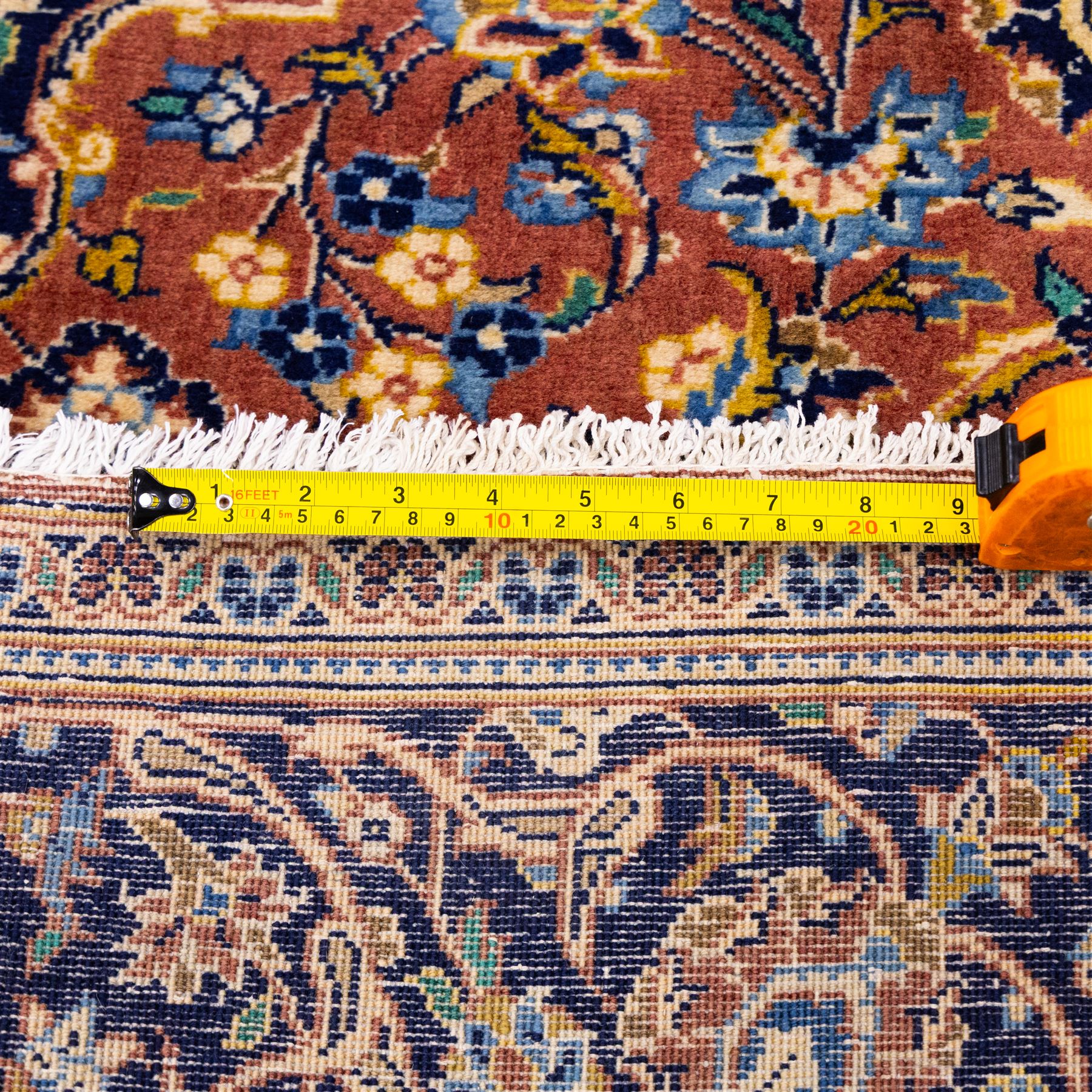Central Persian Kashan hand-knotted rug,  terracotta field with central shaped ivory and dark blue medallion with palmettes, floral sprays and scrolling vine ornament, with conforming corner spandrels enclosed by a broad navy border of palmettes and flowering vine between multiple guard stripes, with cotton fringe ends 