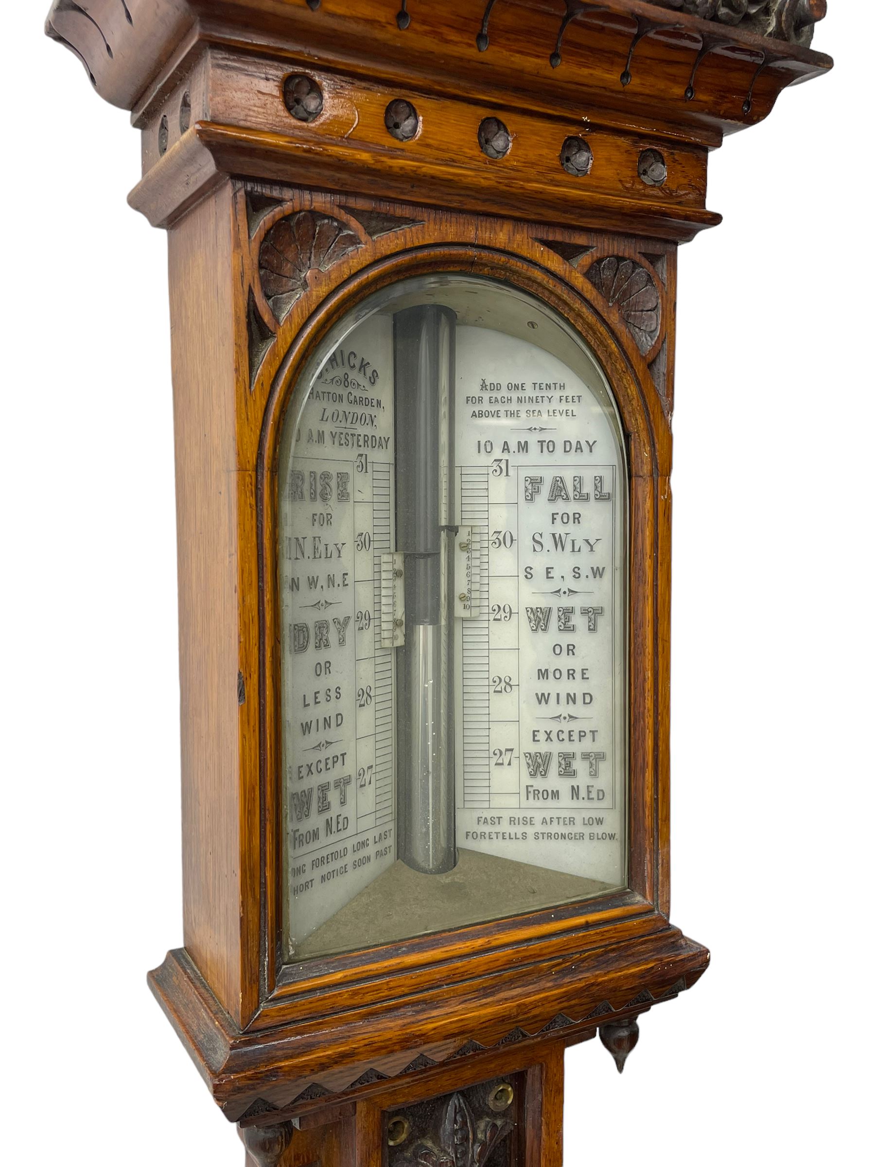 J Hicks - Hatton Garden London, - late 19th century carved oak cased Fitzroy barometer in a richly carved case with a carved crested pediment and square cistern cover, inverted opaline register reflecting FitzRoy's predictions and a scale from 27 to 31 inches of barometric pressure, with a thick bore cistern tube and adjustable rack and pinion twin vernier, fitted with a glazed snail bulb mercury thermometer recording the air temperature in both Fahrenheit and Celsius. Mercury clean and present.
James Joseph Hicks was born in Ireland, however, early in his life he moved to London where he was apprenticed to the instrument maker Louis P Casella. In 1860 he went into business in his own right as a scientific instrument maker at 8 Hatton Gardens. In 1864 he was granted membership to the British Meteorological Society and exhibited instruments at the Royal Society Exhibitions between 1876 and 1913. Hicks was one of London's most prolific and eminent barometer makers. 
