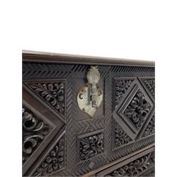 Early 20th century carved hardwood kist or mule chest of small proportions, moulded rectangular hinged lid over foliage carved geometric lozenge panels, the frame carved with chevron banding, fitted with two drawers, the drawer fronts carved with extending leaf motifs over a foliage carved lower moulding, on turned feet