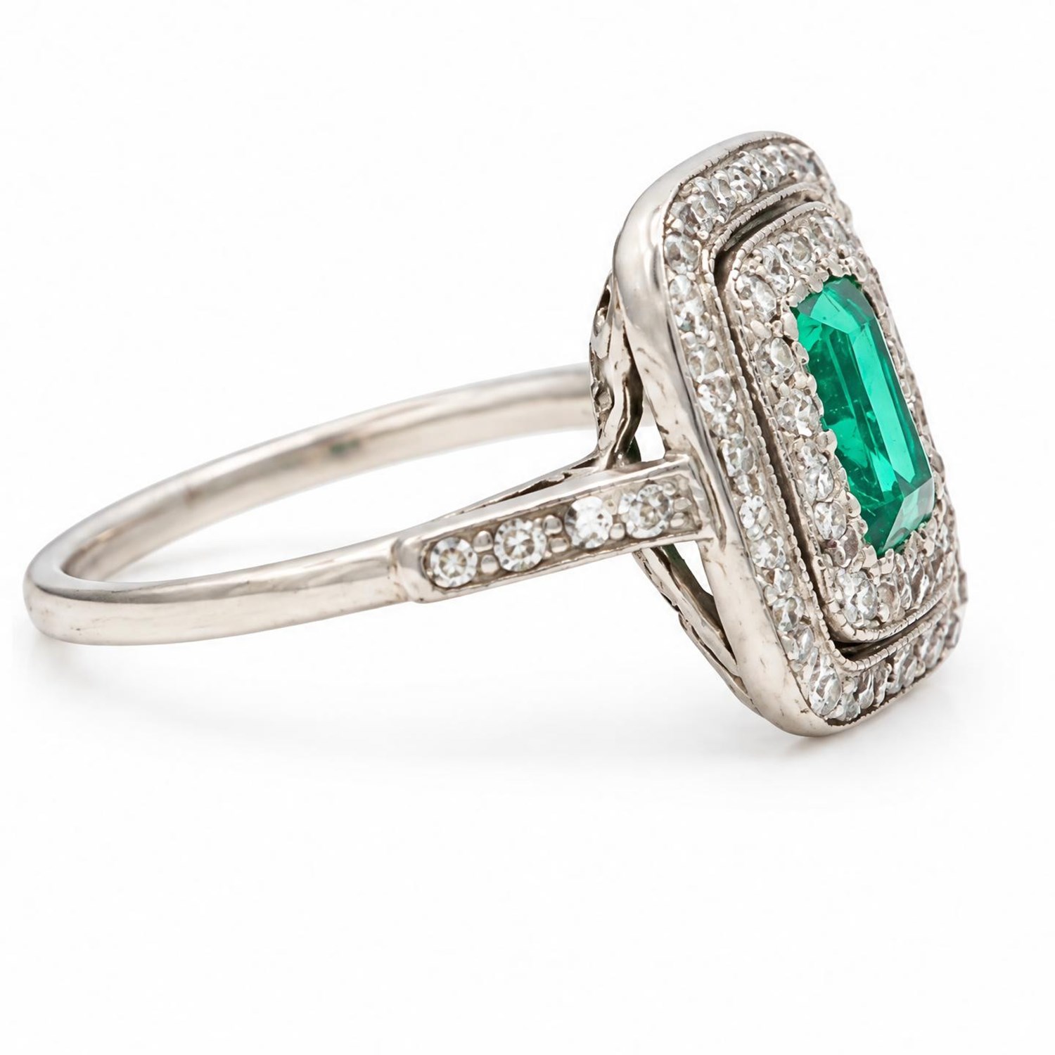 Early 20th century palladium emerald and diamond halo cluster ring, single rectangular cut emerald of approx 0.30 carat, surrounded by two rows of milgrain set diamonds and diamond set shoulders