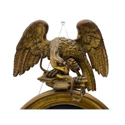 Regency circular giltwood and gesso wall mirror, the large eagle with serpent in talons on naturalistic base, circular frame with foliate decoration and moulded ebonised inner slip, plain glass plate, mounted by scrolled foliate lower carving 