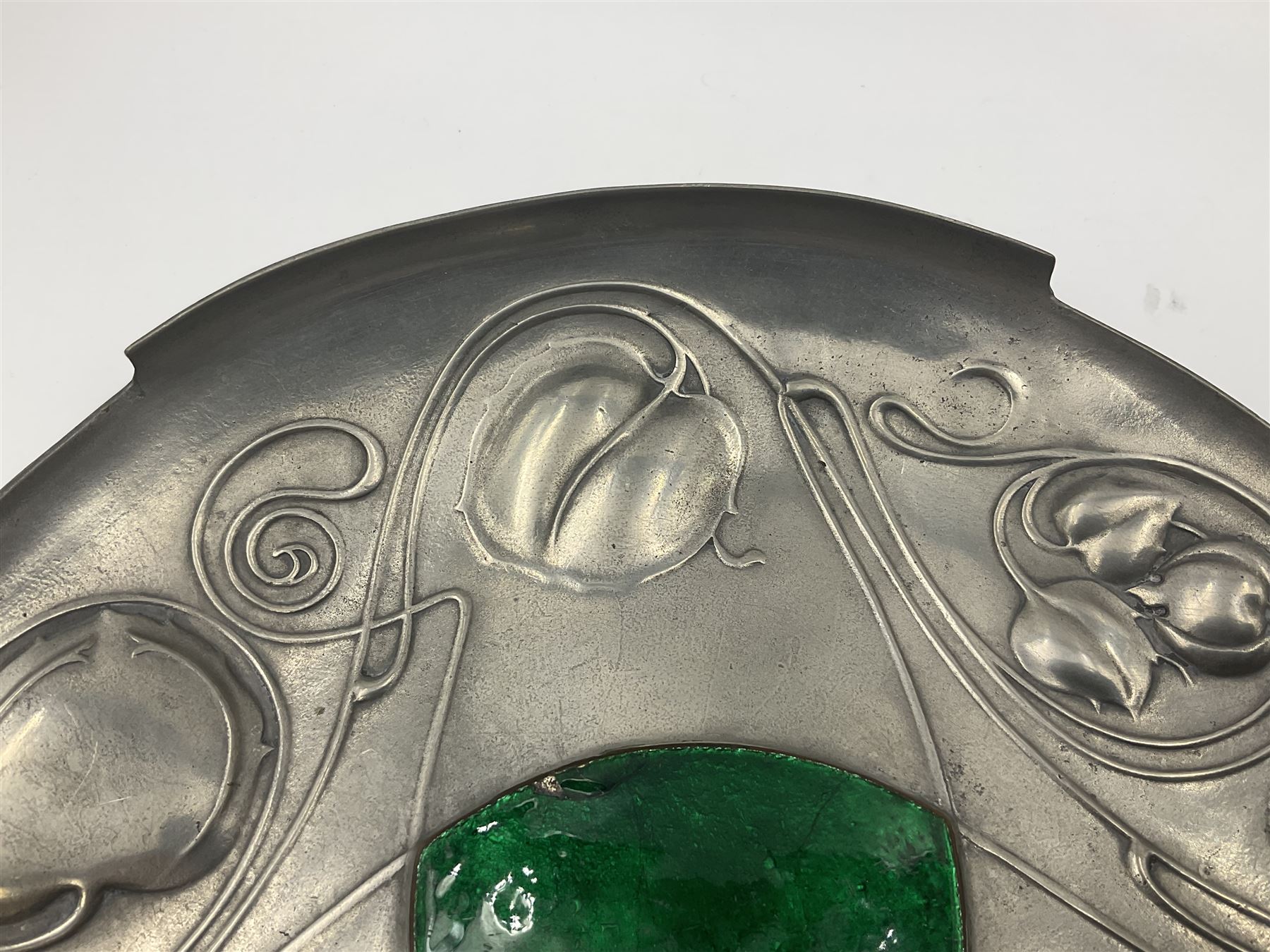 Liberty & Co Tudric pewter Bollelin tray, designed by Archibald Knox, of circular form with shaped edge, cast in relief with foliate tendrils surrounding a green enamel cartouche, impressed beneath Made by Library & Co English Pewter 044, D25.5cm