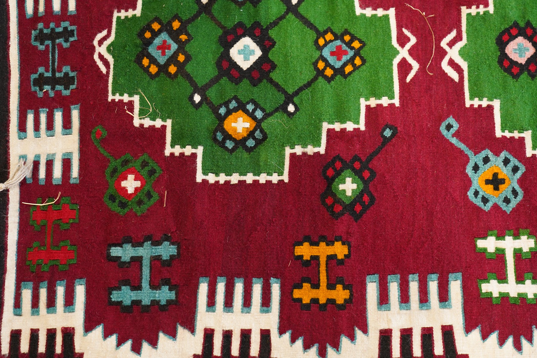 Persian Fars province crimson ground kilim rug, decorated with two rows of geometric emerald green motifs containing stylised plant designs, enclosed by an ivory and dark indigo guard band