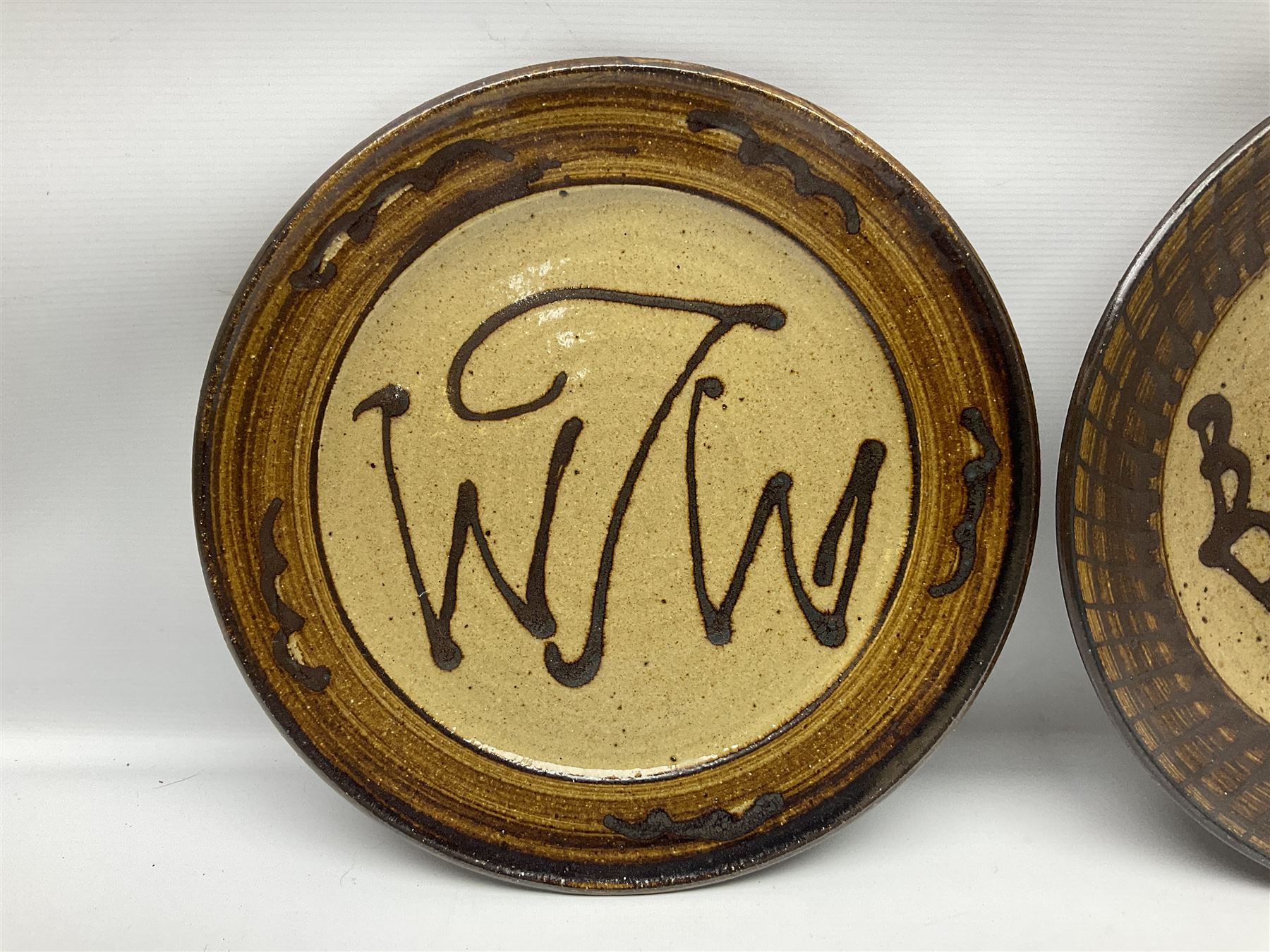 Michael Leach (British 1913-1985) for Yelland pottery; two large glazed stoneware plates with dark brown stylised decoration upon oatmeal ground, together with a jug in merging blue, green and brown, all with impressed marks beneath, largest plate D37cm