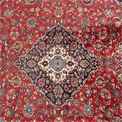 Persian Ardakan carpet, brick red field with ivory and navy central medallion, surrounded by stylised lotus blossoms and cloudband motifs, framed by rich indigo borders featuring palmettes, serrated leaves and angular vine work, woven in the city of Ardakan in central Iran
