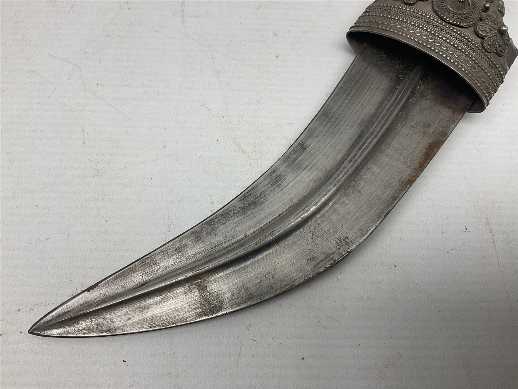 Omani Khanjar dagger, the 19cm curved blade with pronounced medial rib to either side, waisted hilt with dome shaped pommel and silver covered horn grip decorated with filigree bands, floral motifs and beadwork; in an intricately filigree decorated silver and leather scabbard with silver rings woven into the belt mount and fitted with original silver thread-work belt L34cm overall belt length 94cm