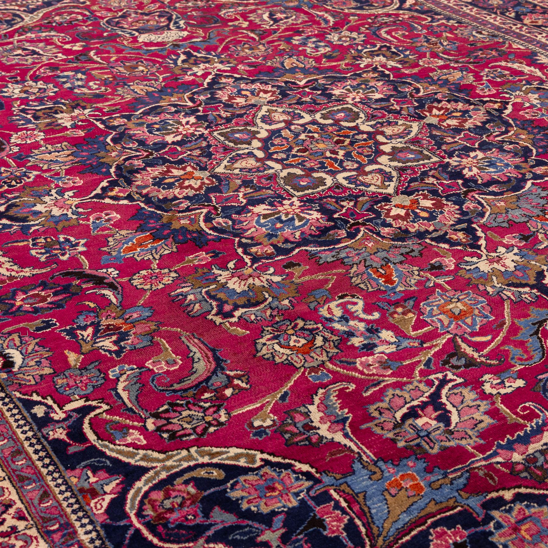 North East Persian Mashad hand-knotted carpet, rich madder red field with central cusped foliate medallion with issuing scrolling arabesques, palmettes, and floral sprays, enclosed within a broad indigo main border of bold palmettes, between multiple guard stripes, with cotton fringe ends 
