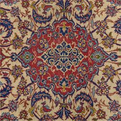 Kashan design wool rug, with red floral medallion on a cream field, decorated with scrolling foliate motifs in blue, red and green tones, enclosed by red and blue floral borders with fringed ends