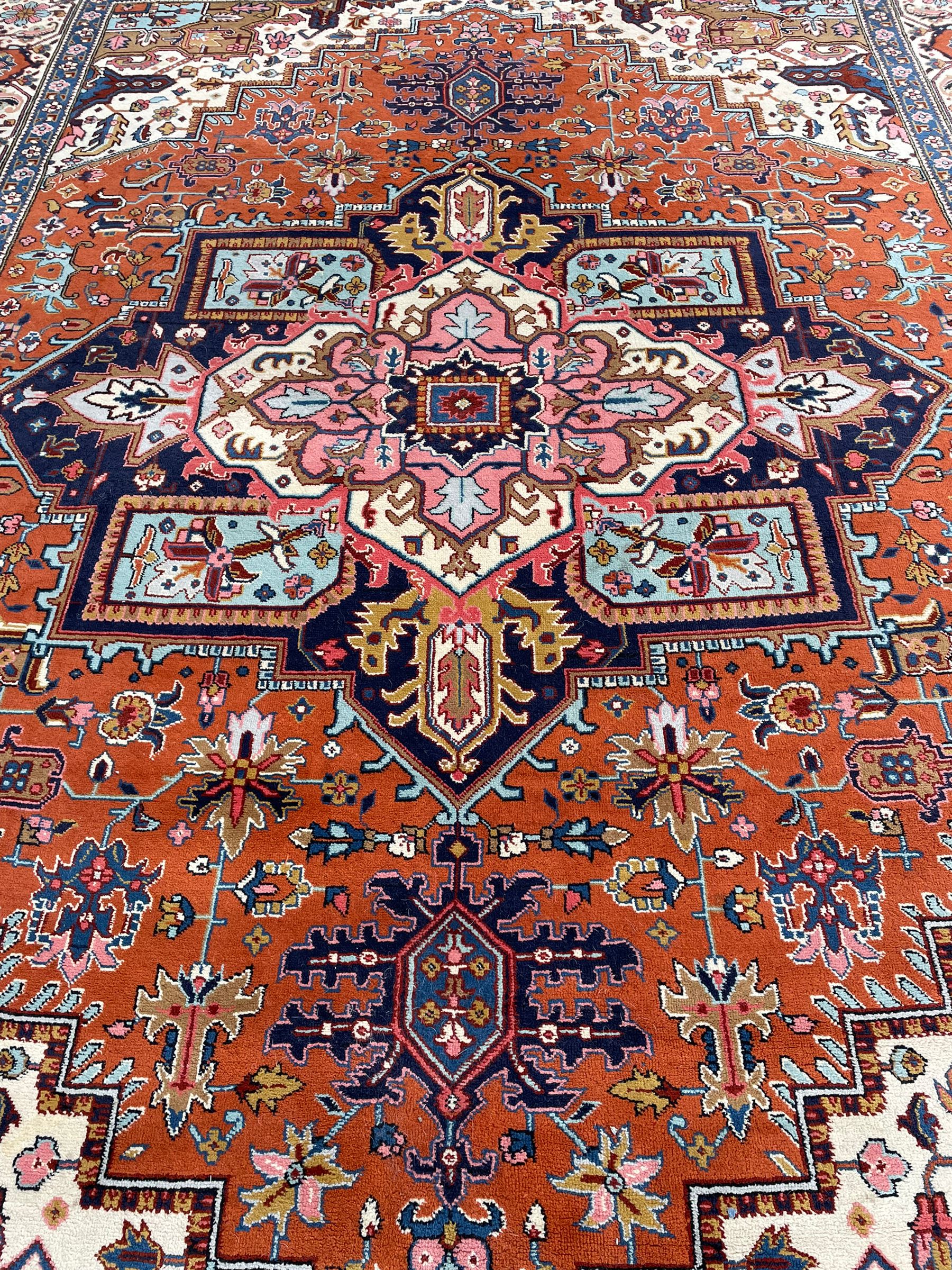 Large Persian carpet, the geometric and stylised floral medallion on rust ground field decorated with stylised plant motifs, guarded ivory border with repeating pattern