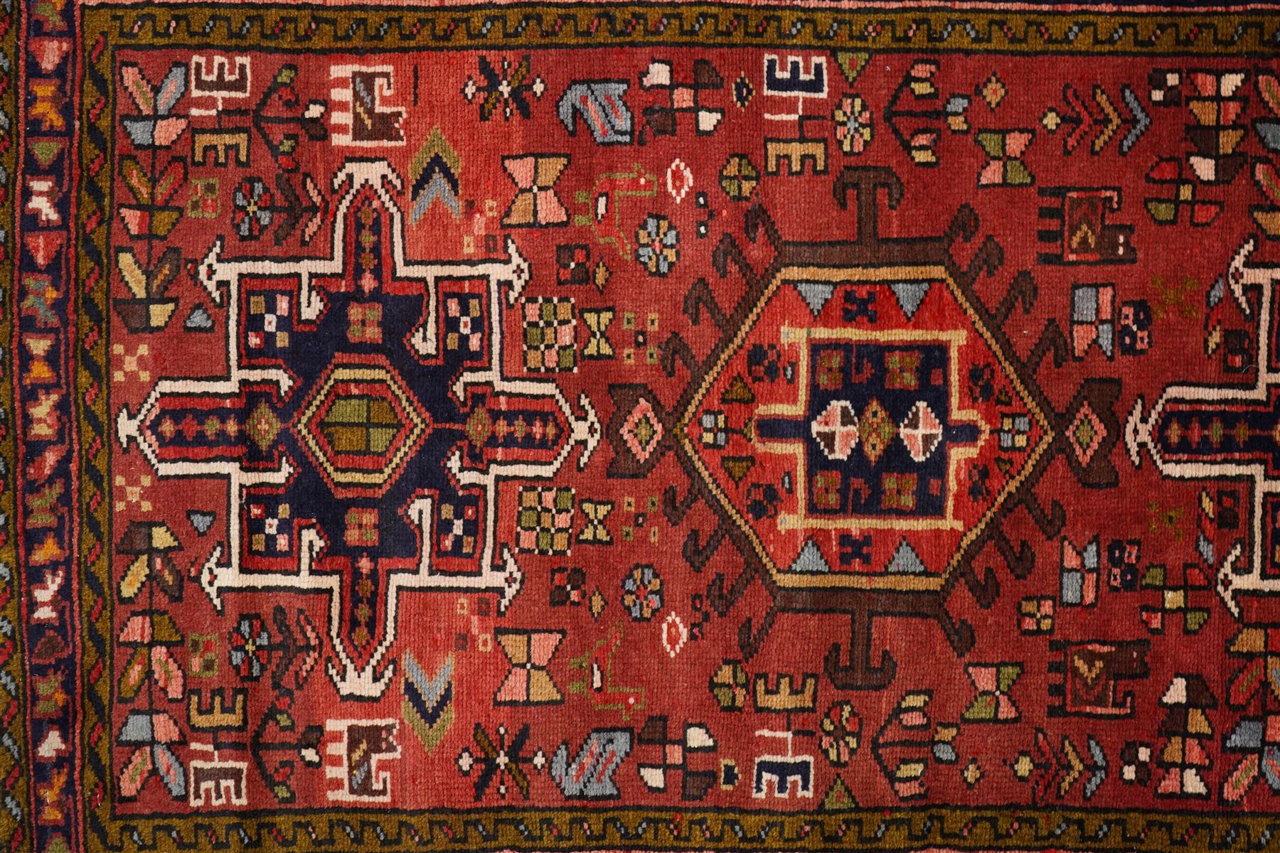 North West Persian Karajeh hand-knotted runner, madder red field with a series of shaped hexagonal medallions and cruciform motifs each enclosing geometric rosette devices linked by angular vine elements, field populated with stylized tribal ornaments, within narrow multiple borders decorated with repeating angular motifs framed by guard stripes of geometric devices, with cotton fringe ends  