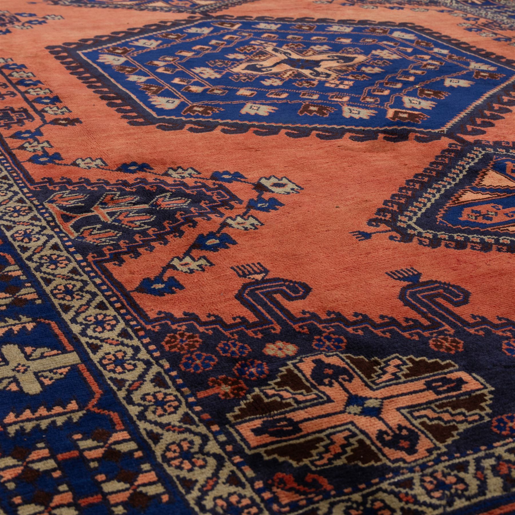 Central Persian Veis hand-knotted carpet, madder red field, decorated with a repeating arrangement of large octagonal and diamond medallions filled with stylized cross and geometric motifs and angular tribal devices within a series of geometric borders in tones of madder red, indigo blue, ivory, and soft green, with cotton fringe ends 