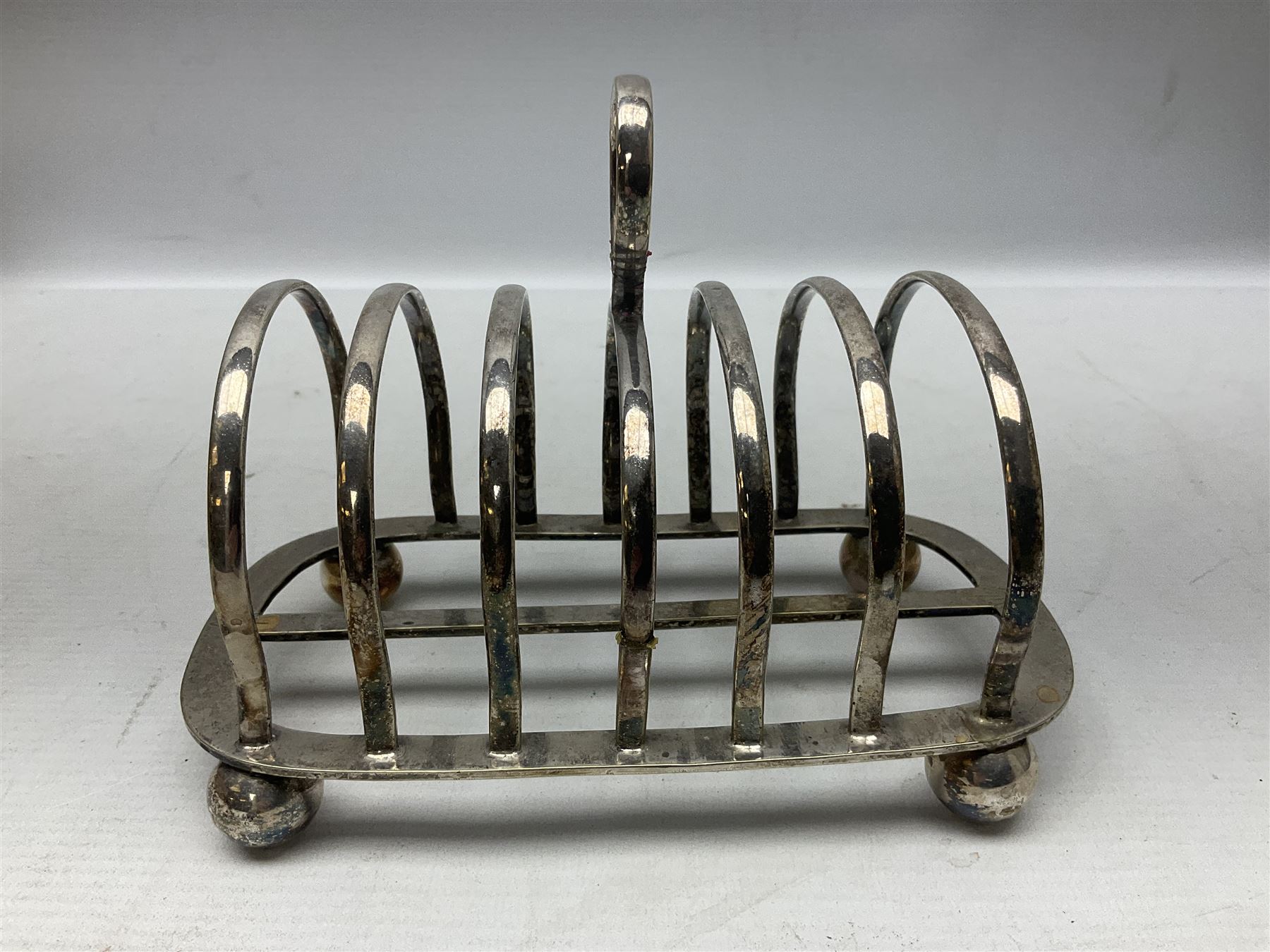 Silver plate seven bar toast rack, of curved form with central ring handle, upon bun feet, H13cm 