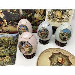 Two ceramic Hummel postcards by Goebel, both displayed on wooden easels, together nine Hummel eggs, set of four Hummel School Days plates, on wooden hanging rack, Goebel Collectors Club Member plaque etc
