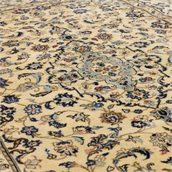 Central Persian Kashan hand-knotted carpet, ivory ground, with a central pale blue shaped floral medallion with pendants, surrounded by scrolling foliate and floral motifs incorporating rosettes, palmettes and delicate vine work in blue, cream and beige tones, enclosed by an ivory border with repeating palmettes and meandering vines, flanked by floral guard stripes, with cotton fringes
