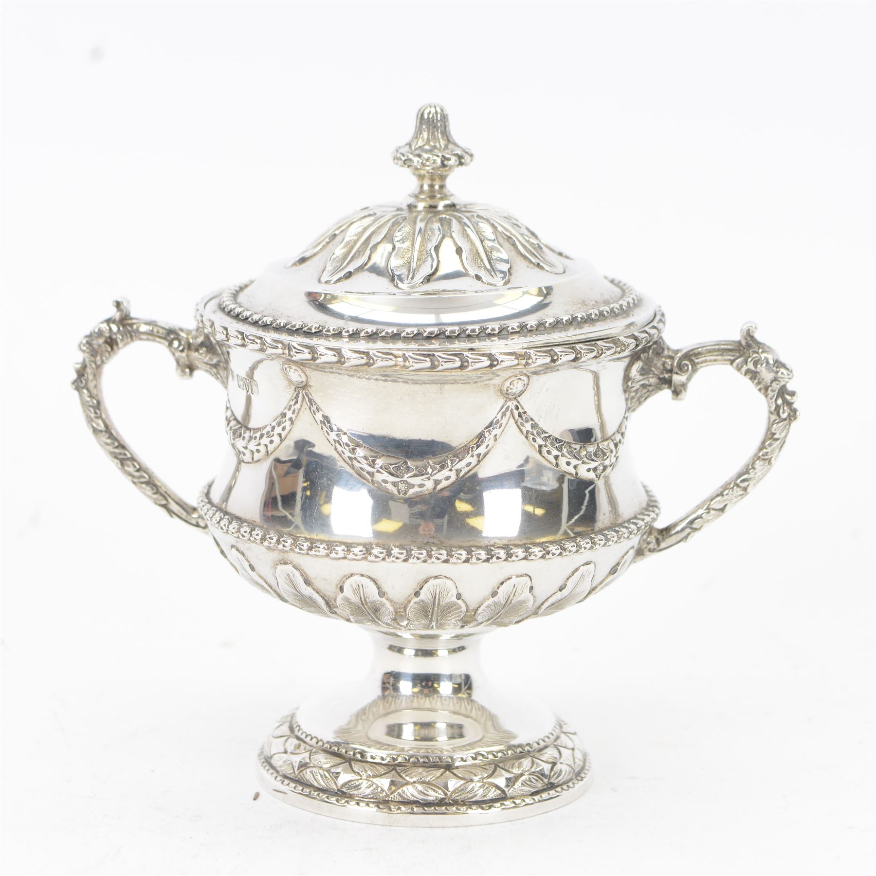 Early 20th century silver twin handled pedestal bowl and cover, the wasted body with embossed husk swag and band, above stiff leaf detailed lower section, and twin zoomorphic mask detailed handles, the slightly domed cover with conforming embossed decoration, upon a spreading circular foot, hallmarked George Nathan & Ridley Hayes, Chester 1908, H15cm
