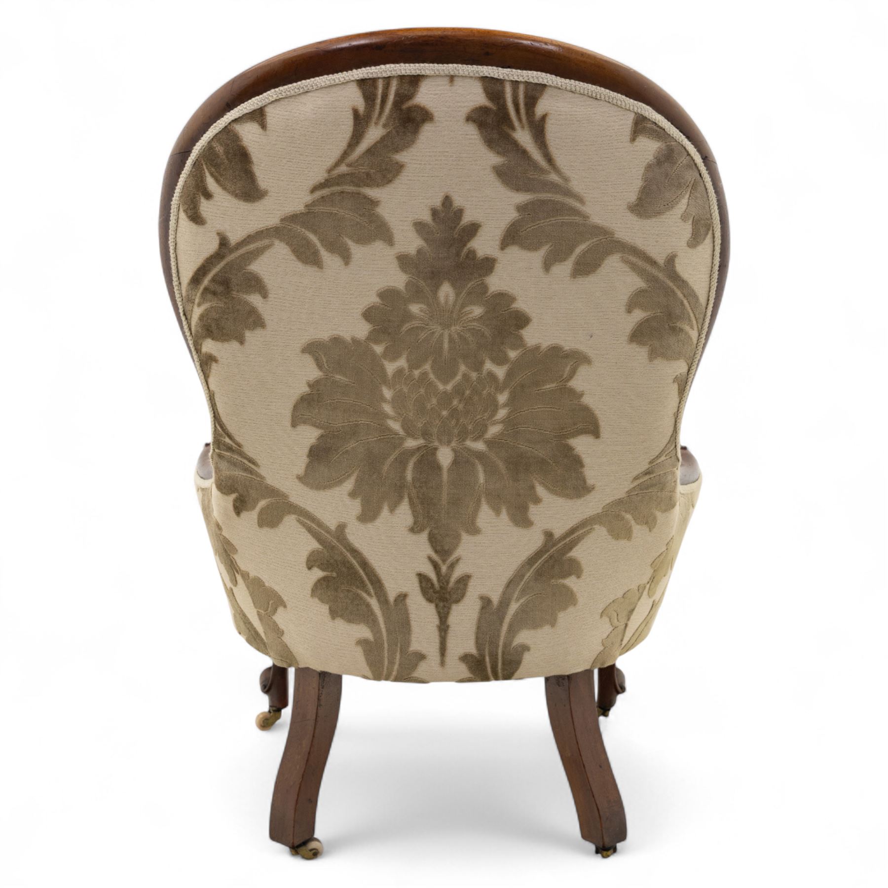 Victorian mahogany framed spoon back armchair, the shaped and padded back over serpentine seat upholstered in a floral damask pattern fabric within a moulded frame carved with scrolled arms, raised upon cabriole front legs with scroll feet on porcelain castors 