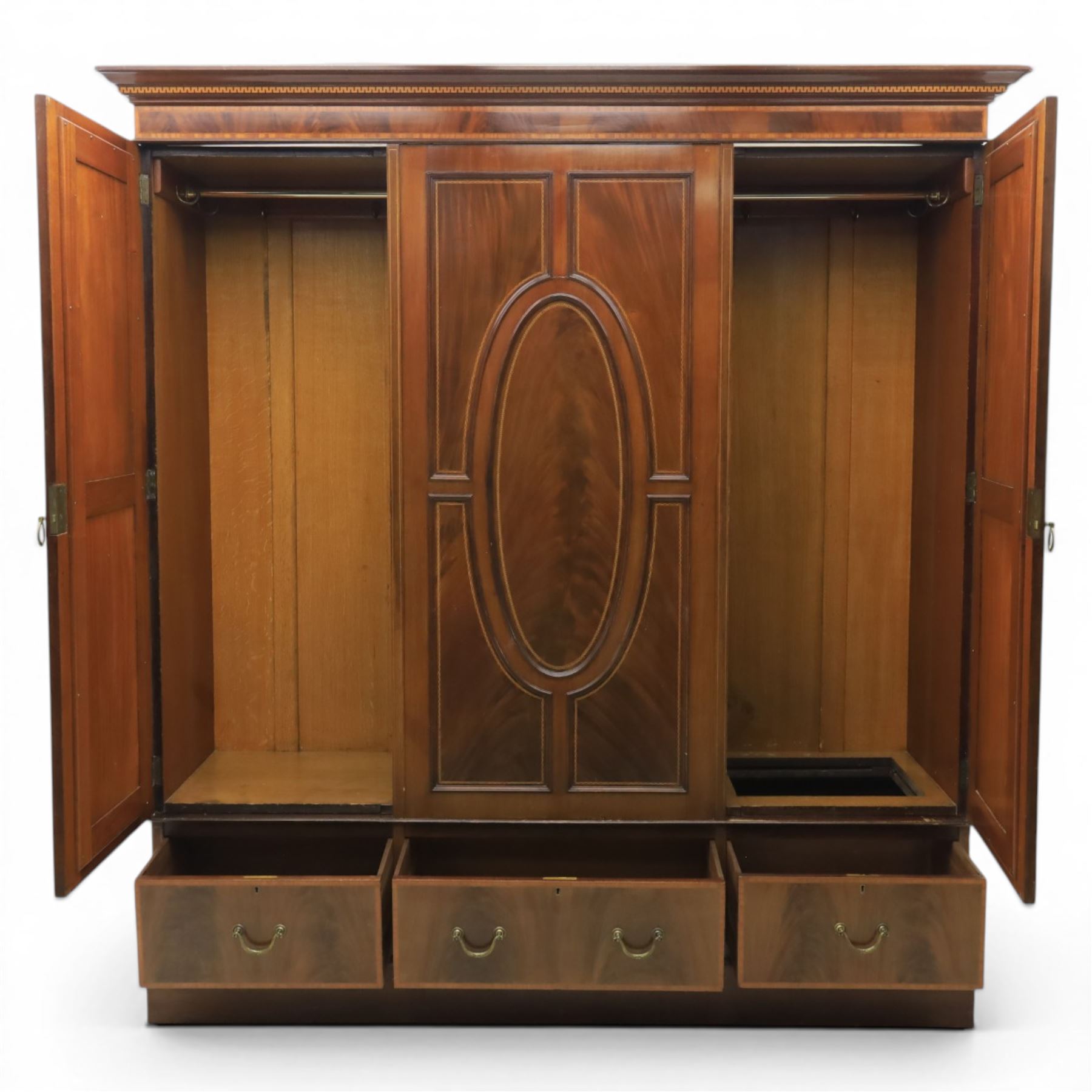 Edwardian inlaid mahogany triple wardrobe, featuring two oval mirror doors with bevelled plates, enclosing central figured veneered panel with mouled detail, above three base drawers