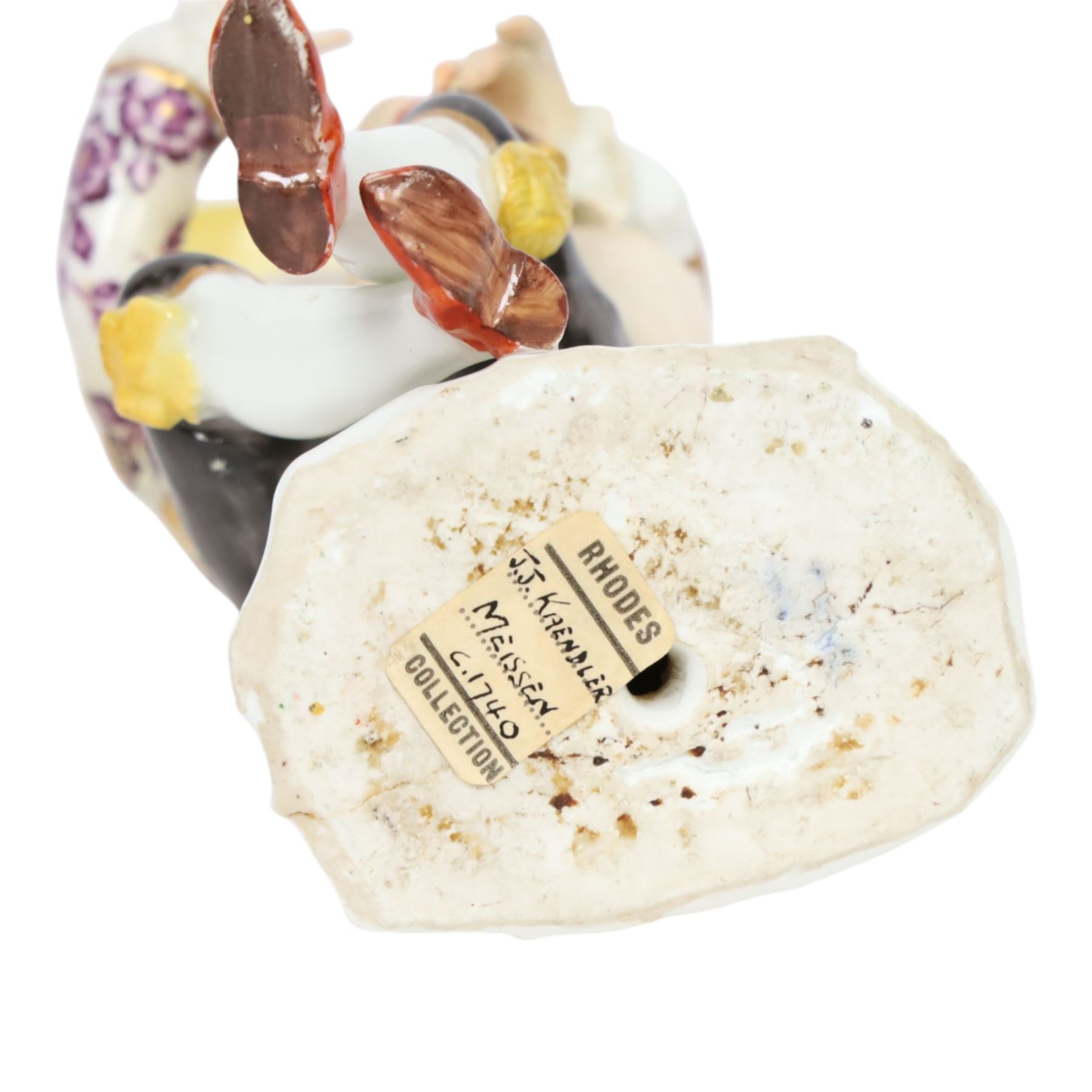 Mid 18th century Meissen figure, modelled as a harlequin playing bagpipes, circa 1745, possibly modelled by J.F.Eberlein after earlier models by J.J.Kändler, wearing a gilt edged tunic painted with flowers, black breeches with rosettes at the knees, red shoes and conical yellow hat, seated upon a rock, with traces of blue crossed swords mark beneath, H14cm