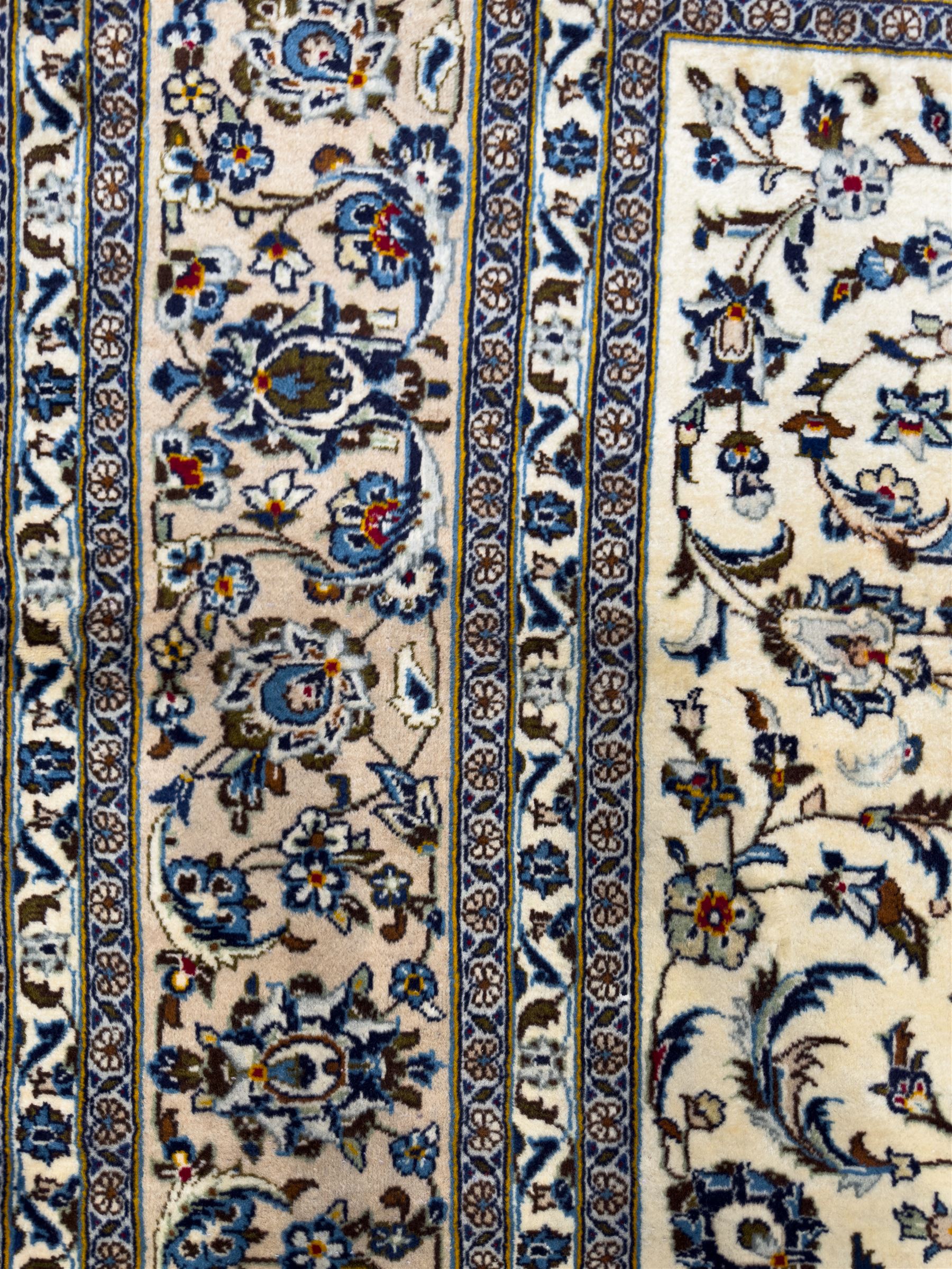 Central Persian Kashan hand-knotted carpet, ivory field with an all-over design of scrolling vines, lotus palmettes, and rosettes in shades of blue and brown within a blue ground border of palmettes and arabesques between multiple guard stripes, 
348 cm x 246cm