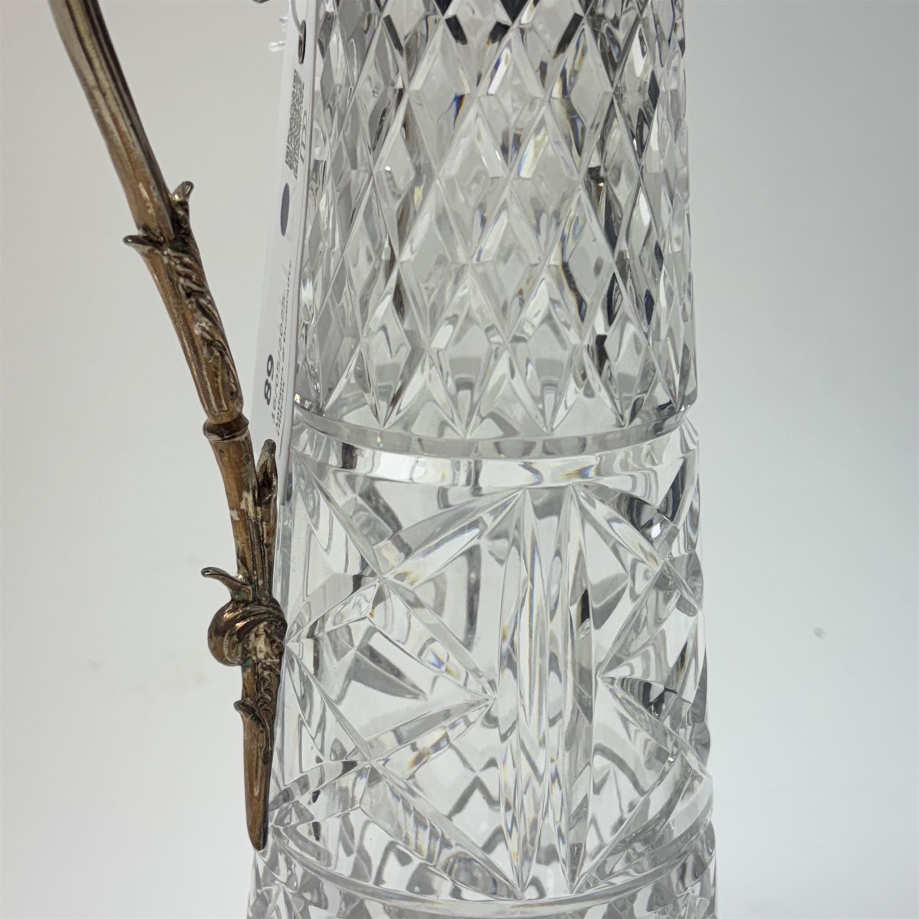 Silver plate mounted glass claret jug, the glass body of tapering form, the hinged lid a lion finial with shield shaped empty cartouche, the collar and spout cast with Bacchus face masks surrounded by grapes and vines, together with another silver plate mounted example, tallest H33cm