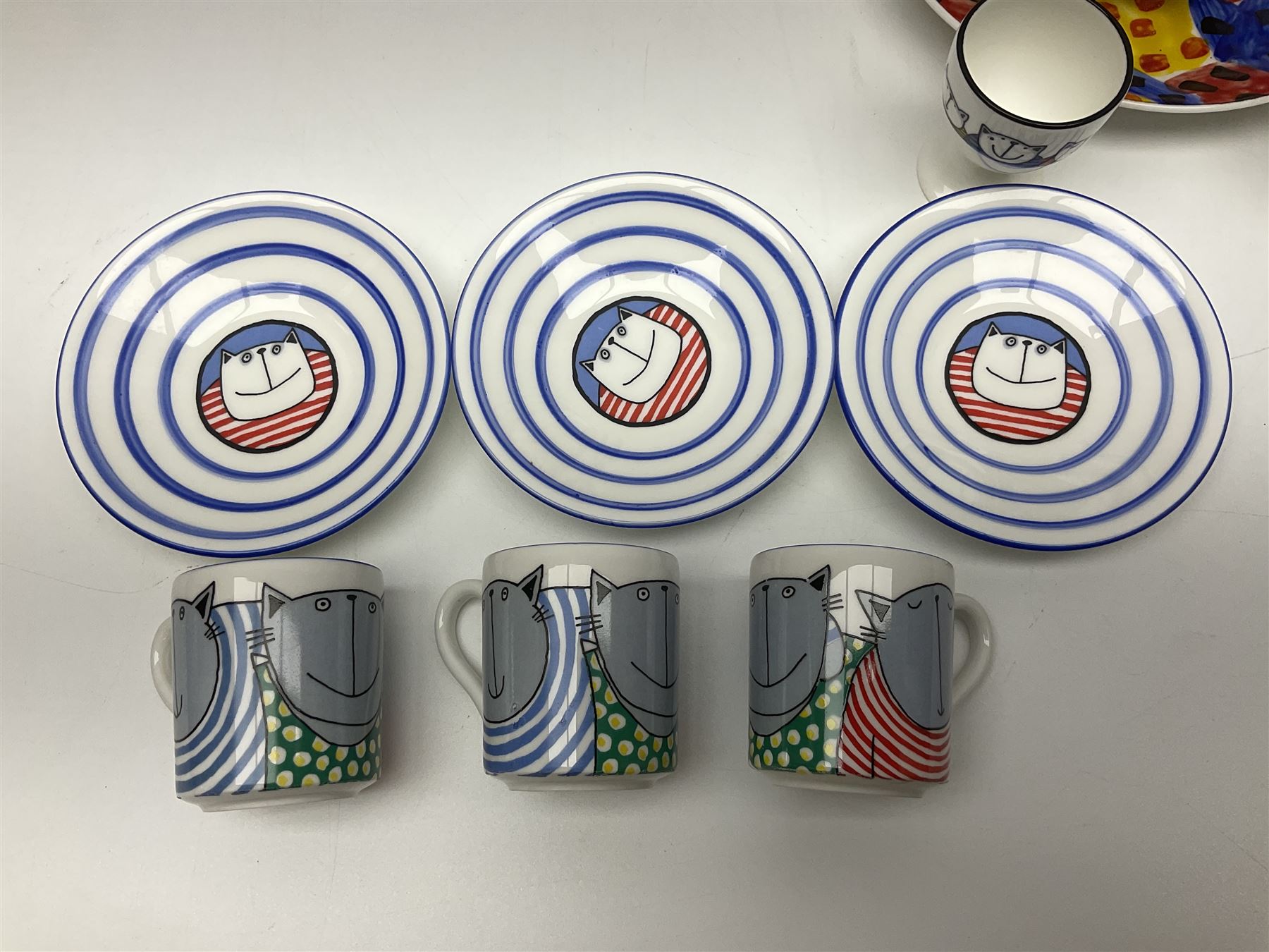 Modern studio pottery by Josie Firmin, to include cup and saucer, three espresso cups and saucers, pair of egg cups etc, each hand painted with varying cartoon cat designs