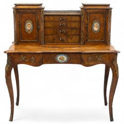 Late 19th-century Louis XV revival gilt bronze mounted and walnut Bonheur-de-Jour, rectangular-shaped serpentine form, with gilt bronze beading, frieze with two blind drawers and gilt bronze handles, centre drawer with large central serves style porcelain plaque, the elevated section with brass gallery above panelled cupboard doors also with serves style porcelain plaques and gilt bronze mounts, interior with single shelf, central section with four drawers each with gilt bronze handles, raised on slender cabriole legs fitted with gilt bronze rococo style masks and sabots