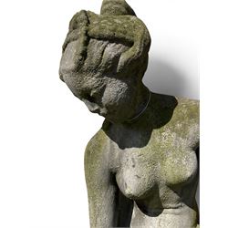 Cast stone garden figure of a classically draped nude female inspired by Aphrodite statues, with stylised up-do arranging her chitin on a circular base, the rectangular pedestal with egg-and-dart moulding over a floral wreath, in weathered finish