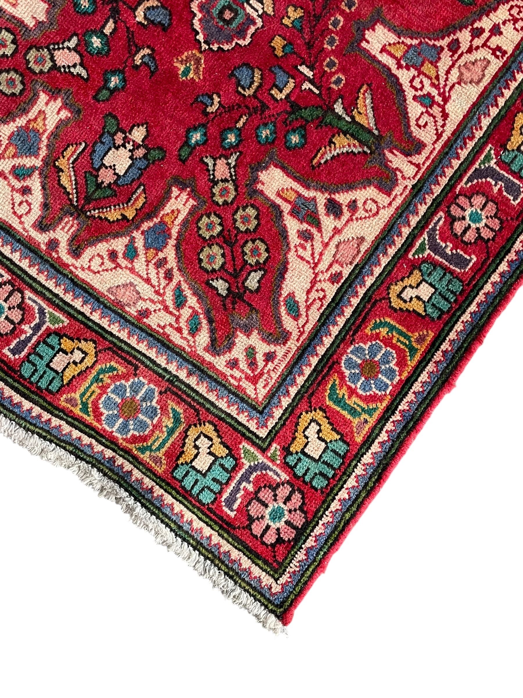 Persian Azerbaijan crimson ground rug, the field decorated with central floral motif and surrounded by trailing floral branches, enclosed within a shaped outer band with further floral decoration, the border with repeating flower heads, geometric guard stripes
