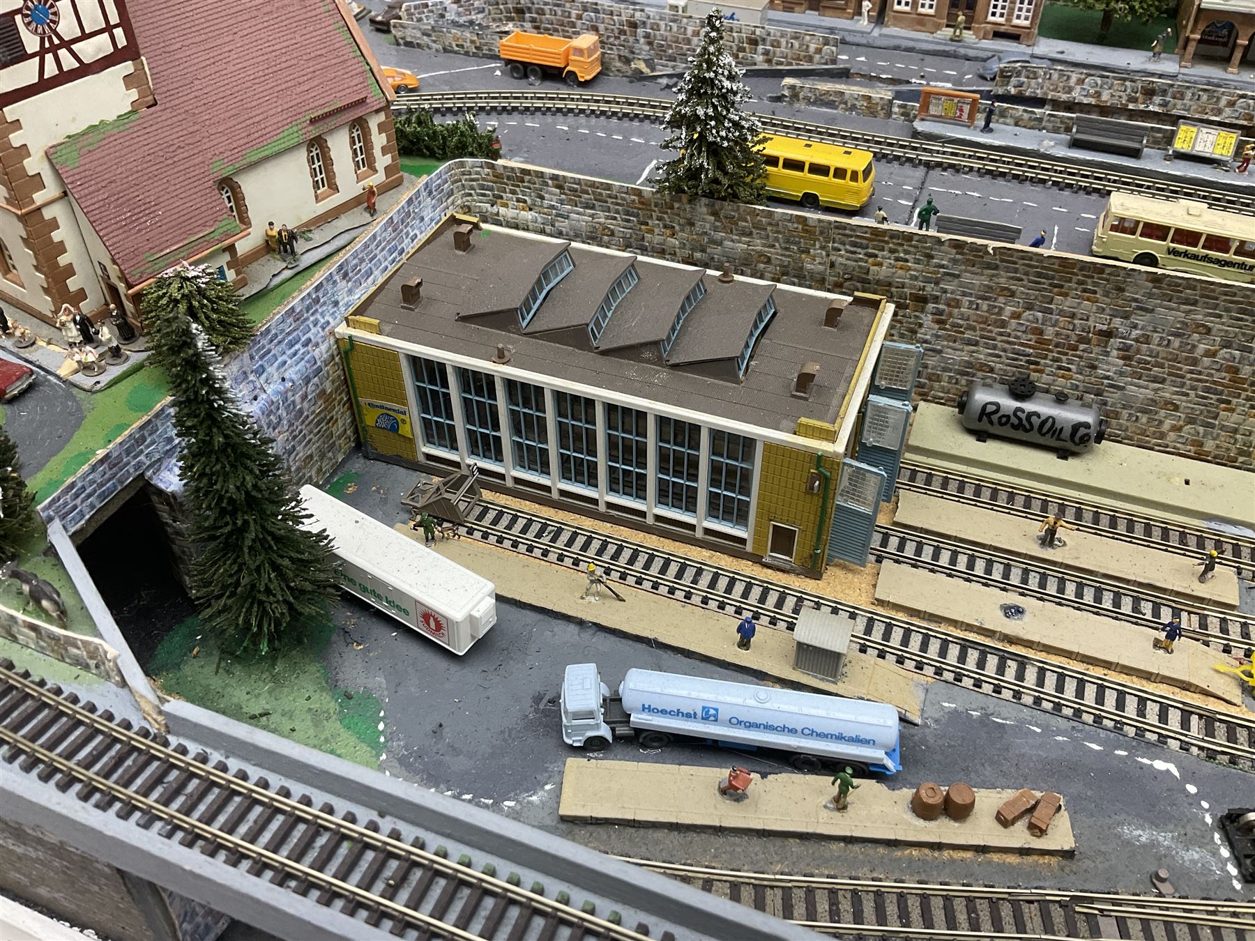 Table top 'N' gauge continental scenic layout as a split level town with various loops of track, station with numerous platforms, engine shed, assorted buildings, roads with motor vehicles and figures, tunnels, trees, river with bridge, tram depot etc 122 x 52cm