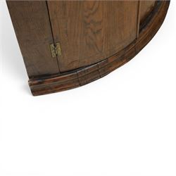 George III oak cylindrical corner cupboard, bow fronted doors revealing a painted shelved interior, brass escutcheons  and hinges, raised on a moulded plinth base