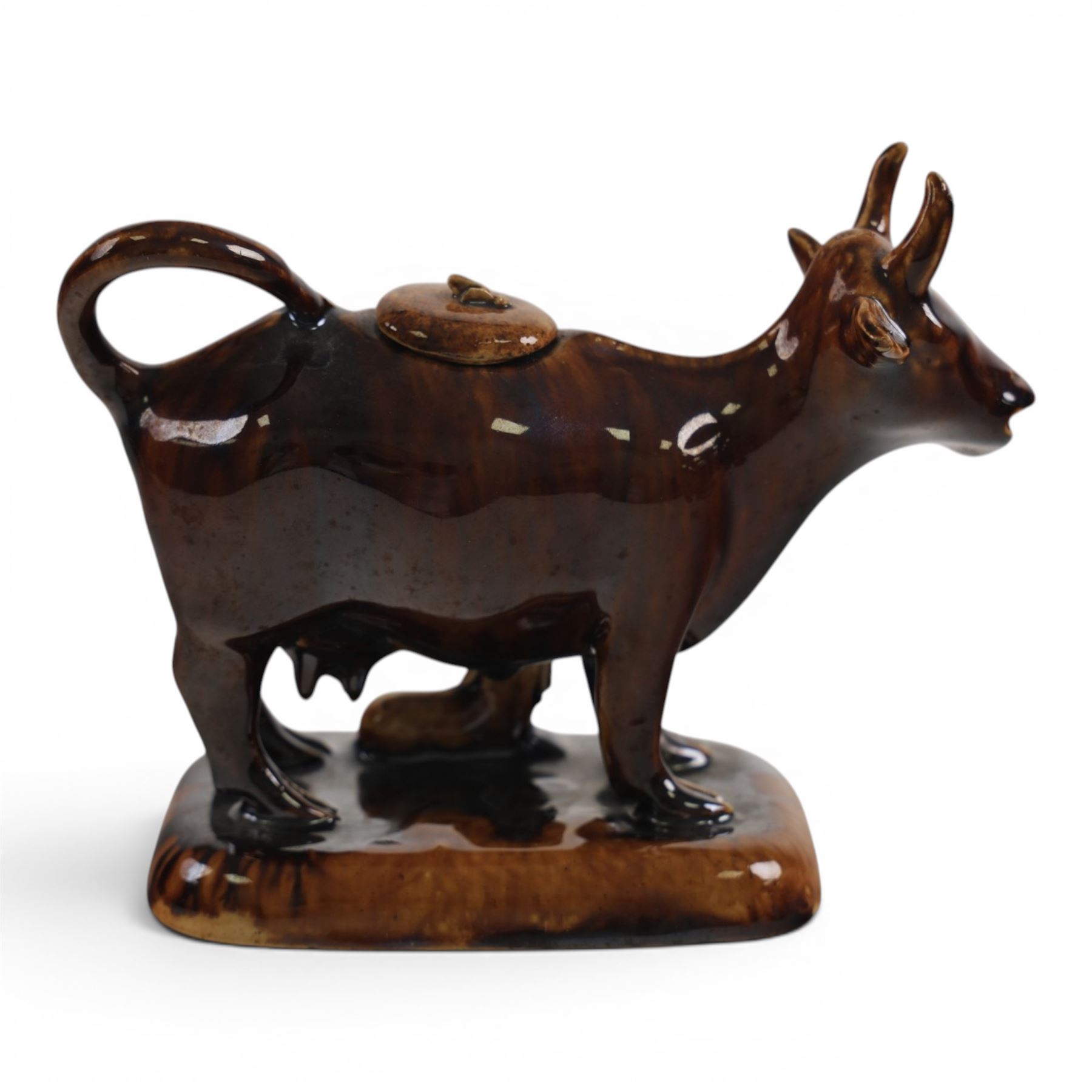 Three Staffordshire cow creamers, one with treacle glaze, the other two painted black and white with a seated figure of a milkmaid, H14cm