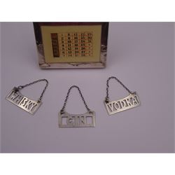 1920s silver mounted perpetual desk calendar, printed in red and black on an ivorine ground, hallmarked Charles S Green & Co Ltd, Birmingham 1925, with wooden easel style support verso, together with a set of three modern silver decanter labels, with cut-out lettering for gin, whisky and vodka, hallmarked London 1982, maker JKM, calendar H8.4cm